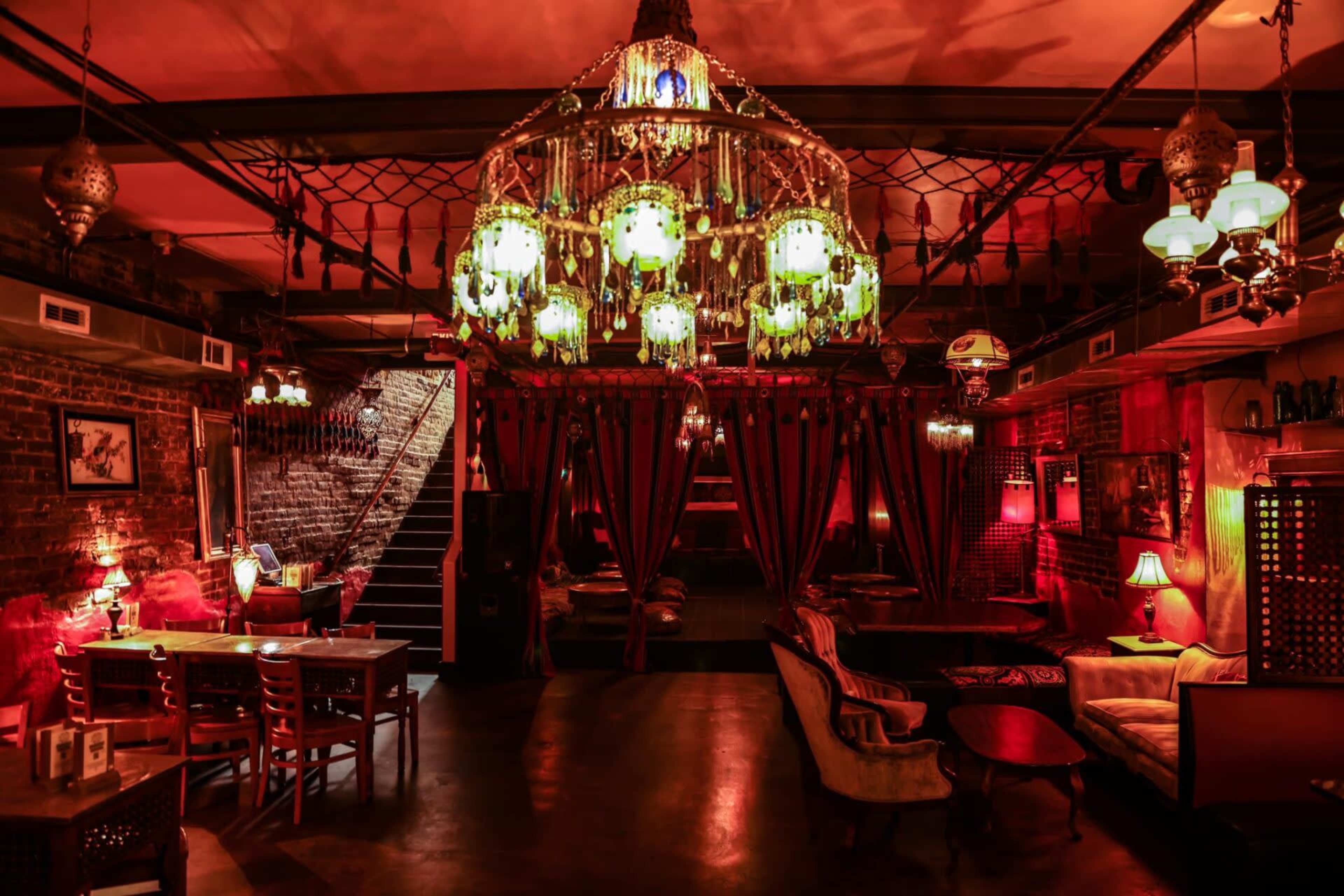 An elegantly designed restaurant interior featuring a large chandelier, vintage furnishings, and warm lighting.