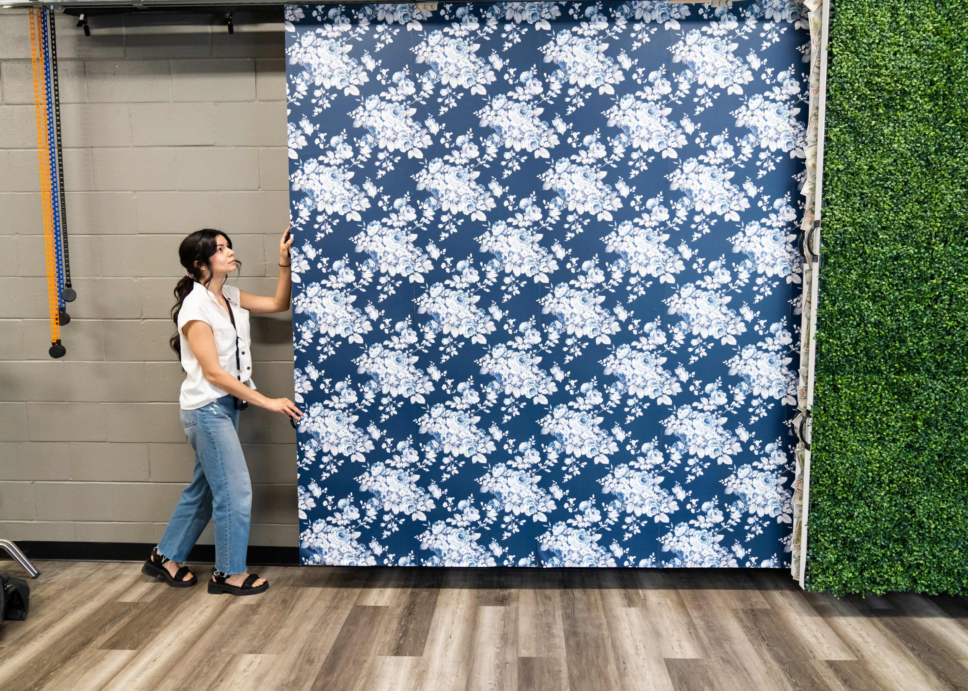 A woman is pulling down a floral-patterned backdrop in a studio space with a green wall.