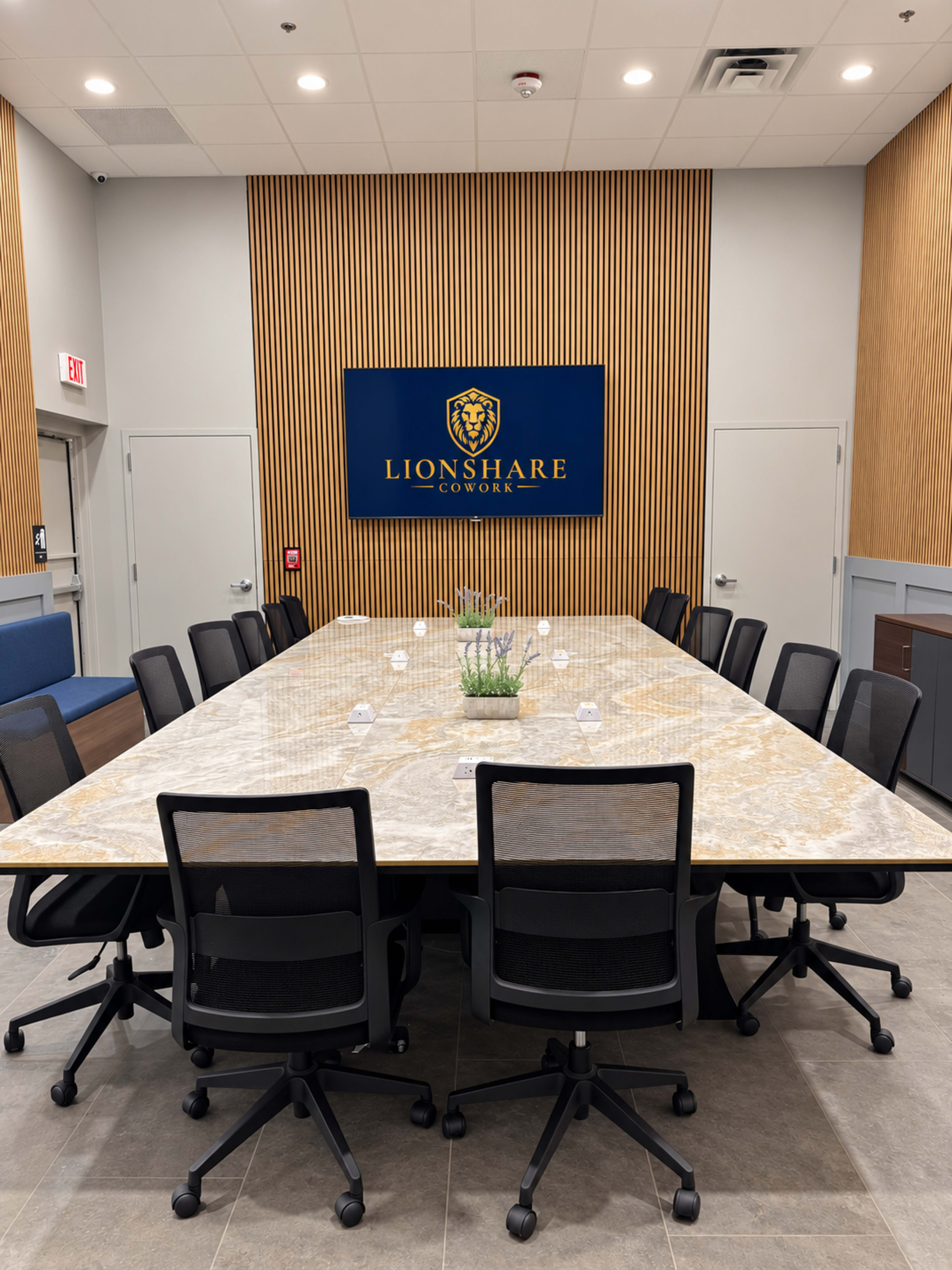 The image shows a modern conference room with a large, rectangular table surrounded by ergonomic chairs, featuring a wall-mounted display with the "Lionshare Cowork" logo.