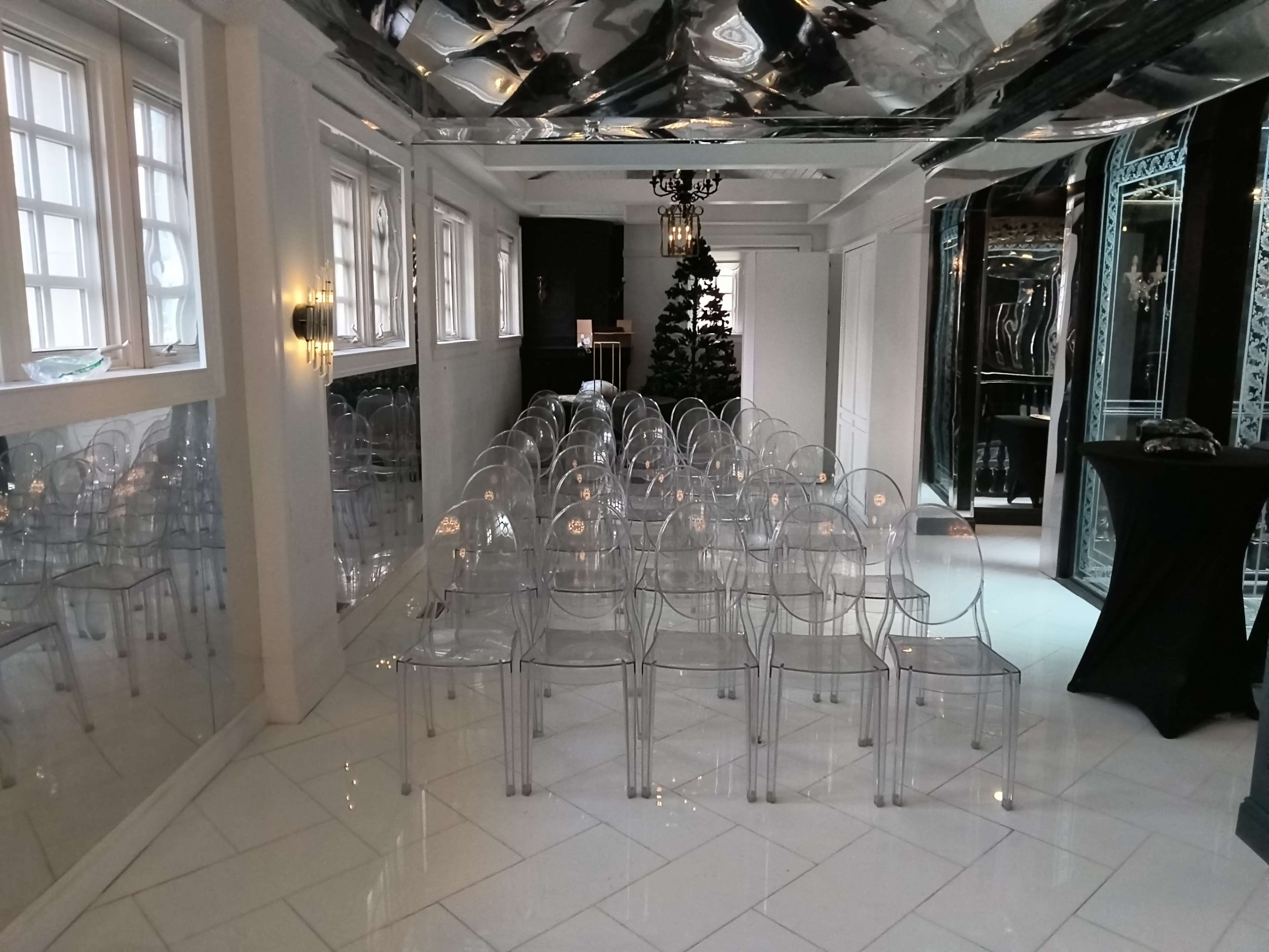 The image shows a room with a mirrored ceiling and clear chairs arranged in rows, with a Christmas tree in the background.