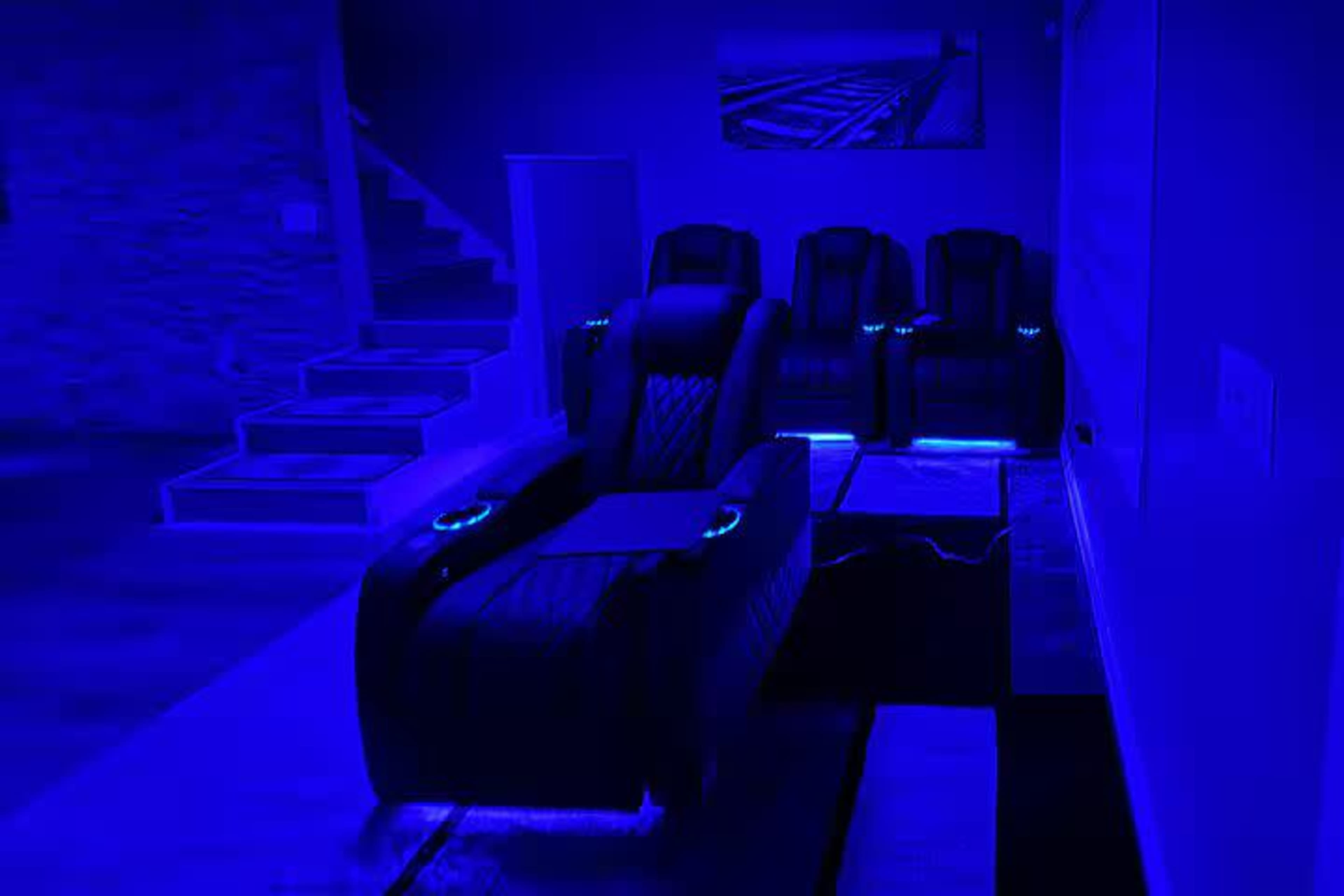 The image shows a dimly lit room featuring several recliner chairs with blue lighting accents and a staircase in the background.