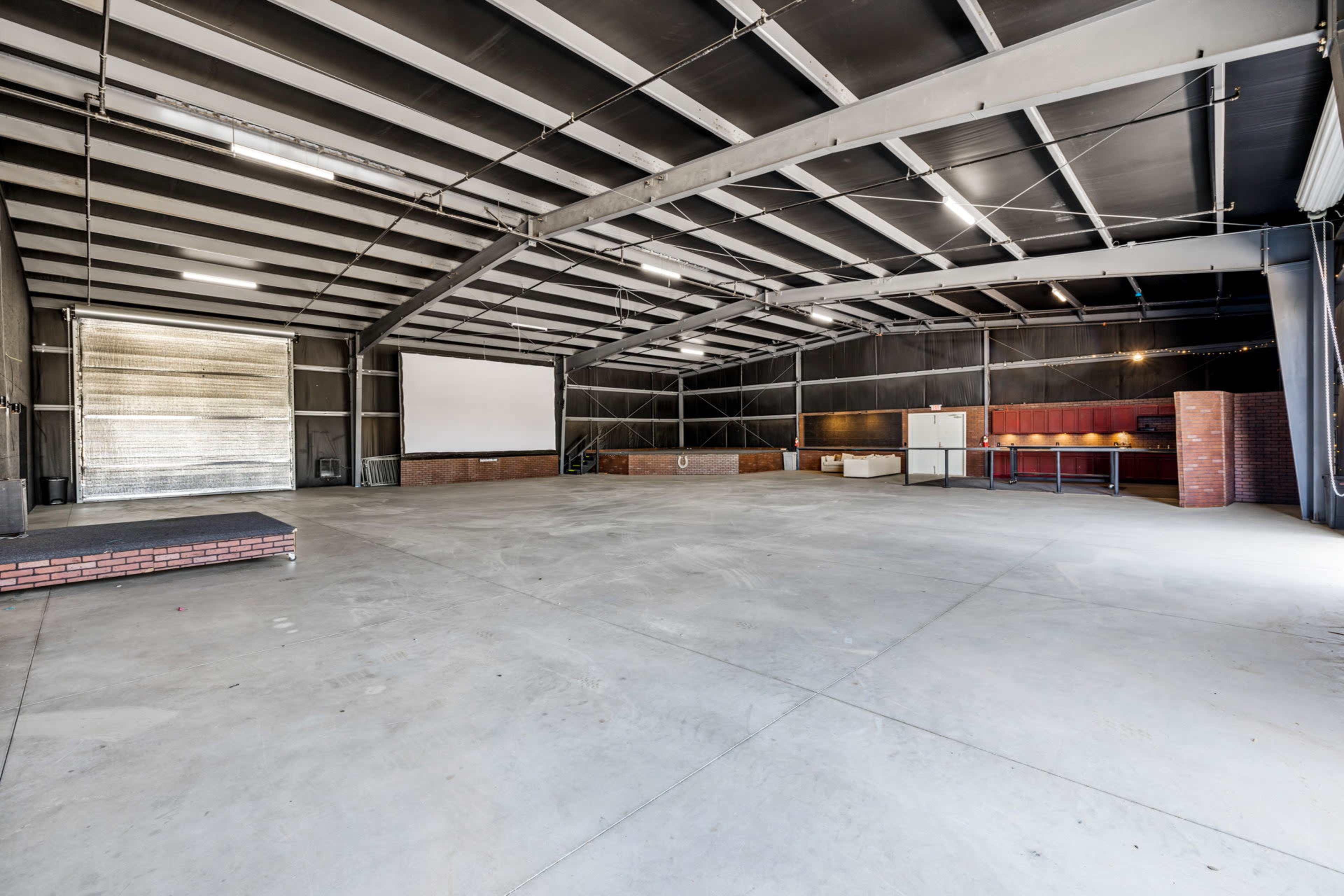 An empty industrial-style indoor space with metal beams, concrete flooring, and a large opening at one end.