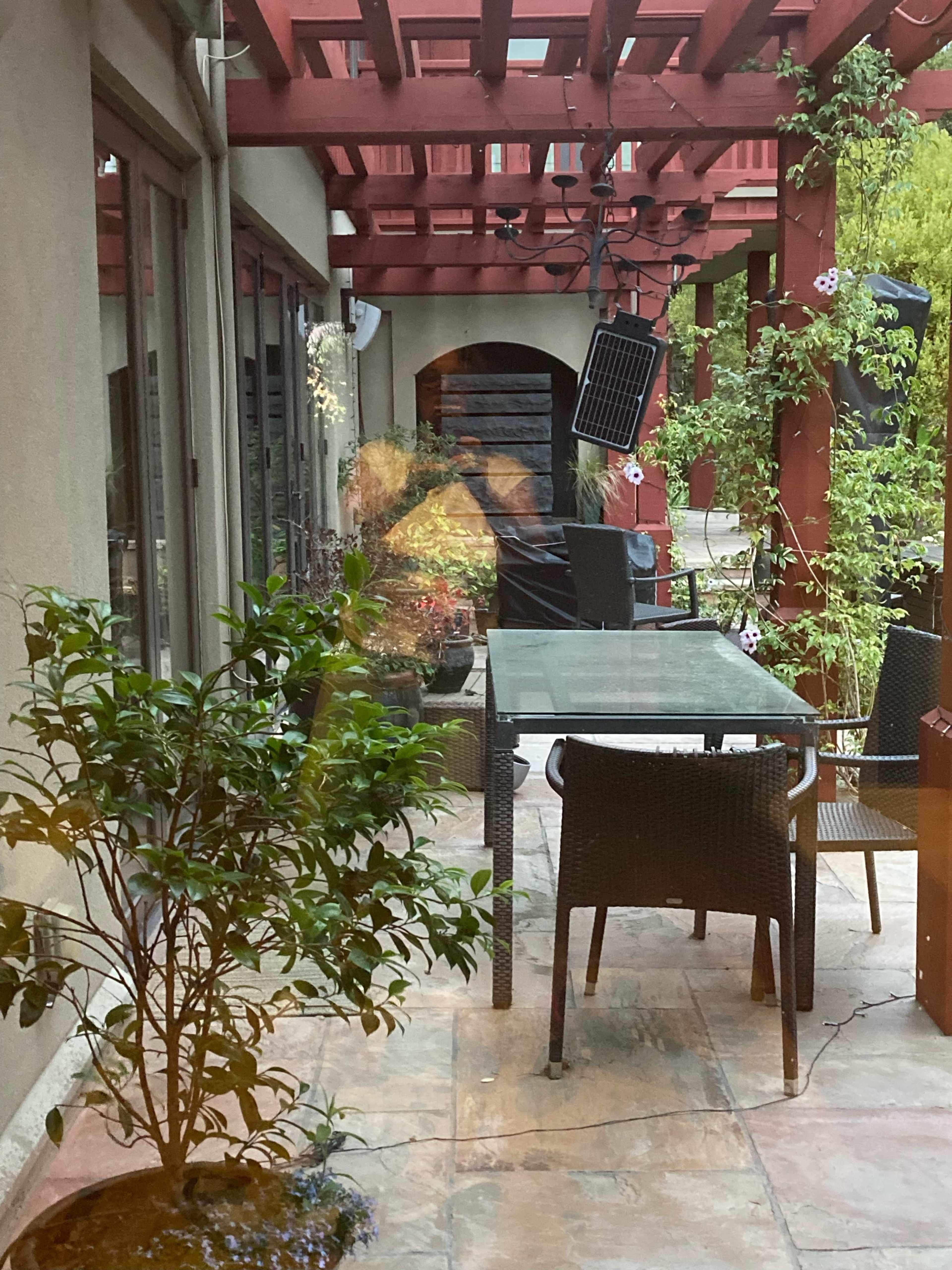 A patio area with a table and chairs, surrounded by potted plants and a pergola overhead.