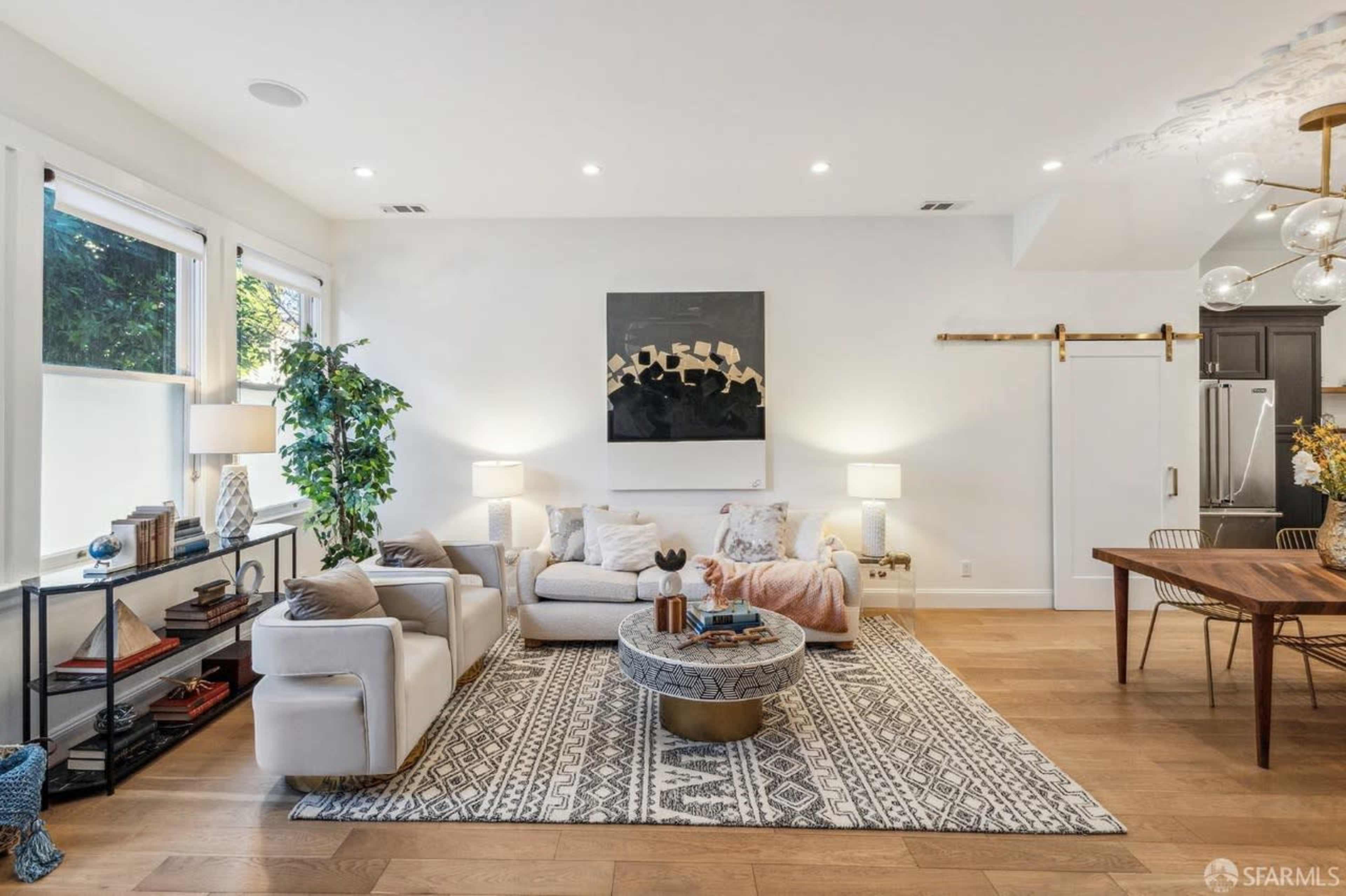 A modern living room features a light-colored sofa, patterned area rug, and elegant decor elements, with a dining table and sliding barn door in the background.