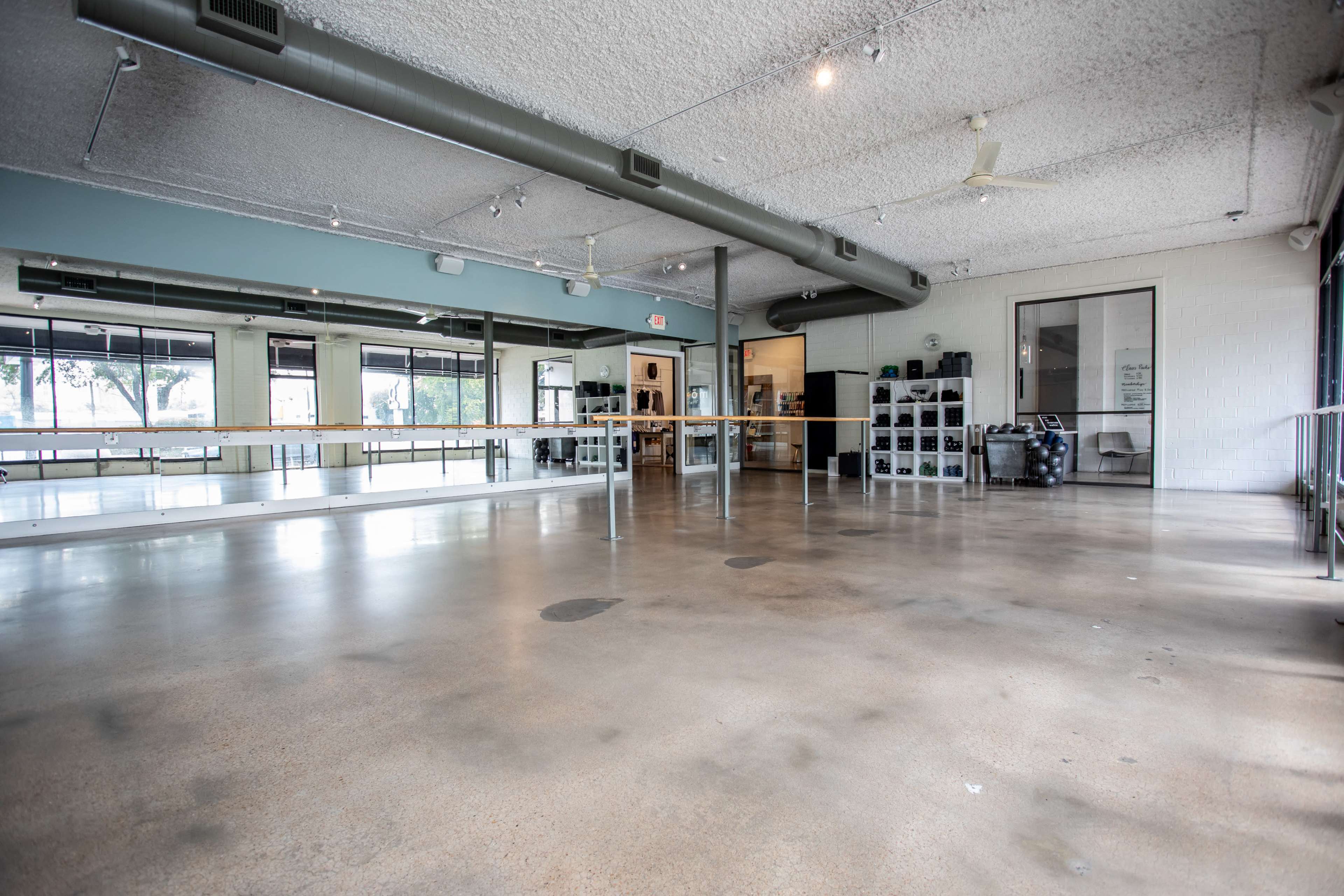The image shows an empty dance studio with a polished concrete floor, large mirrors along one wall, and natural light coming through the windows.
