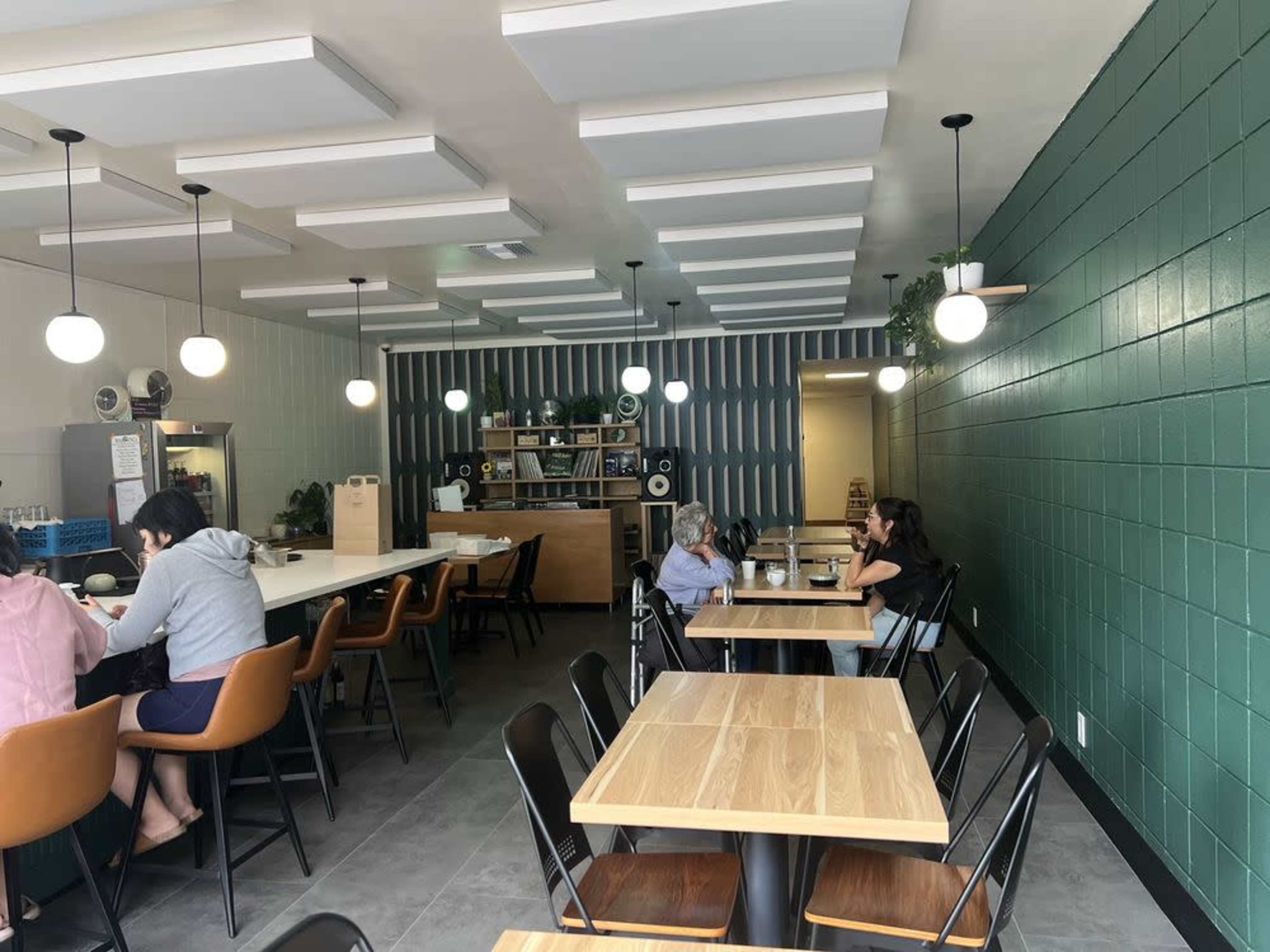 The image shows a modern café interior with green and white walls, wooden tables, and customers seated at tables and a counter.