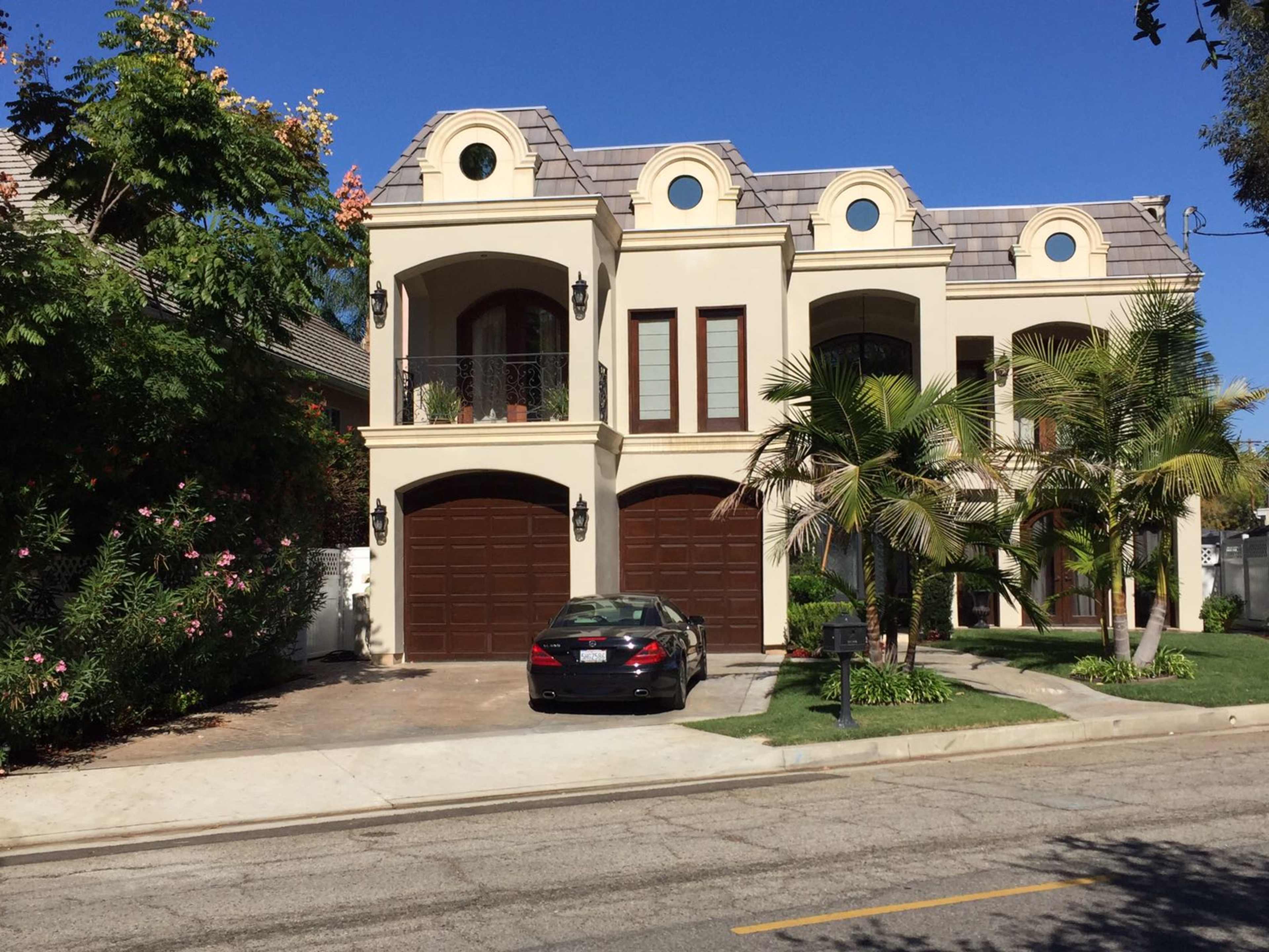 A large, two-story house with a tile roof and a dark sedan parked in front of the garage.