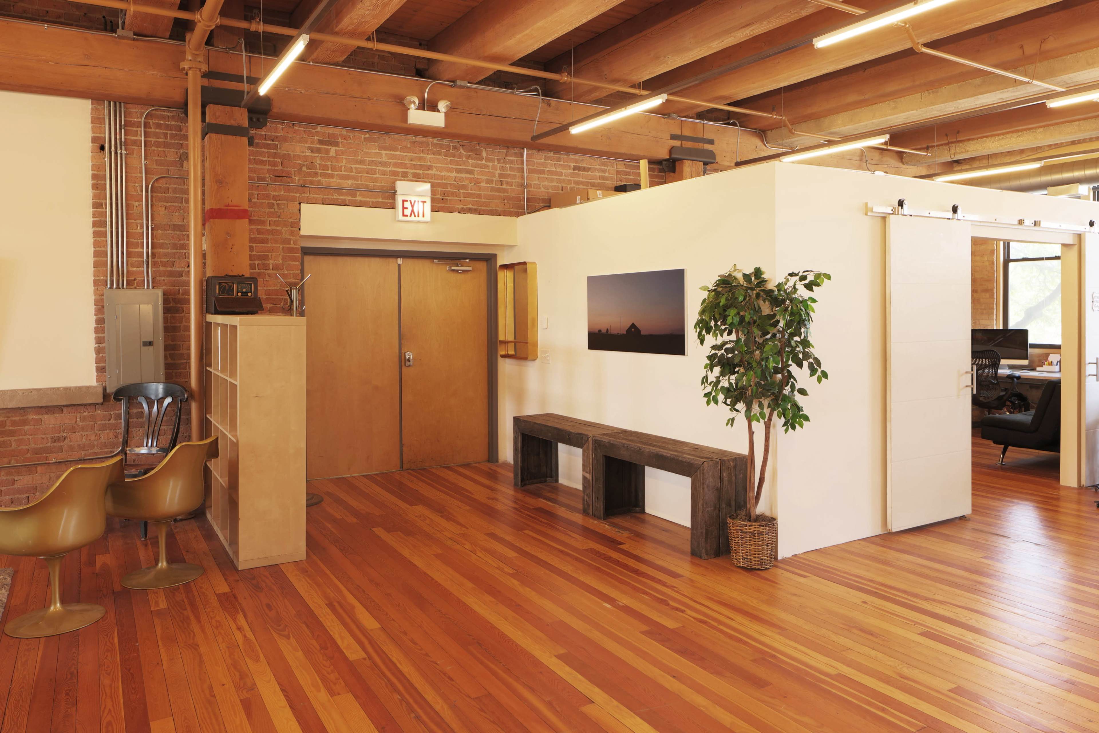 The image shows a modern office space featuring wooden floors, exposed brick walls, and a combination of sliding and double doors leading to different areas.