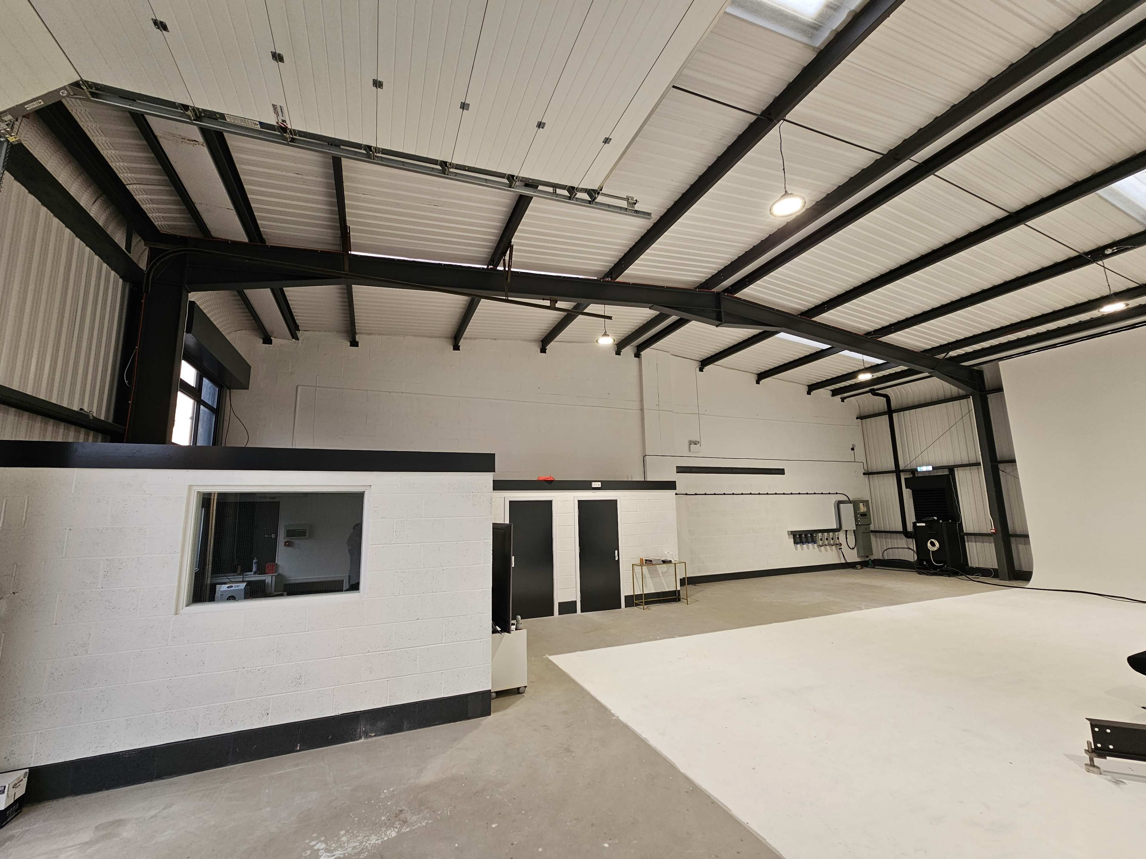 A spacious industrial interior with high ceilings, a concrete floor, and partitioned walls on one side.