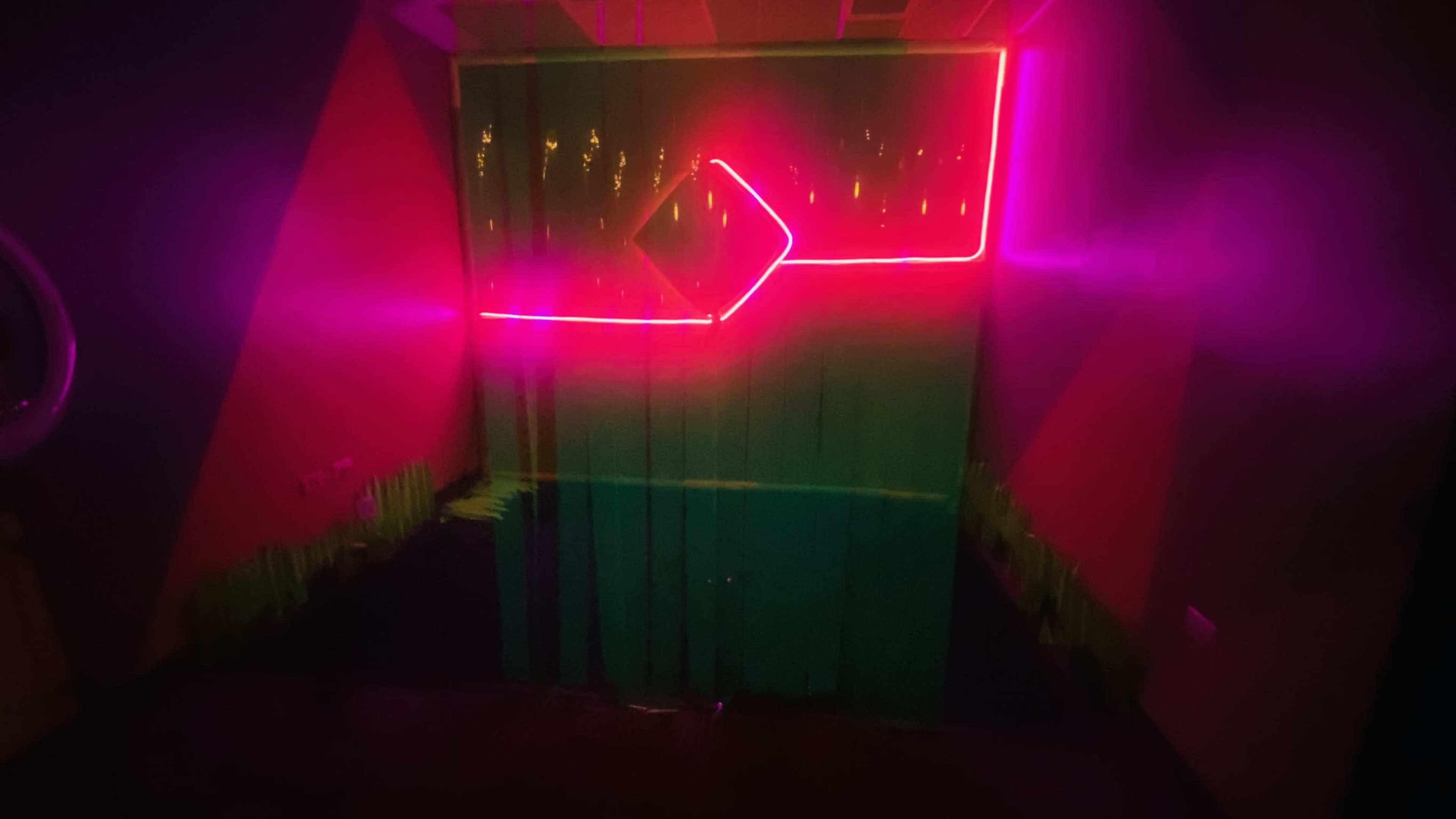 A dark room featuring green and pink neon lights illuminating a backdrop with PVC curtains.