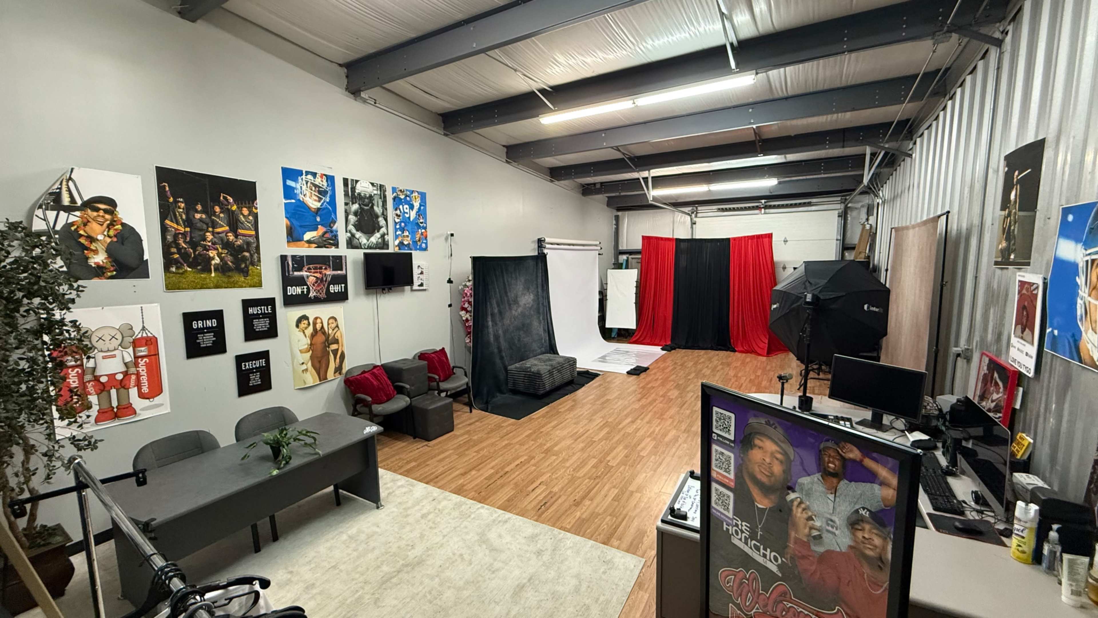 The image shows a spacious studio with various photography backdrops, a seating area with a table and chairs, and several posters on the walls.