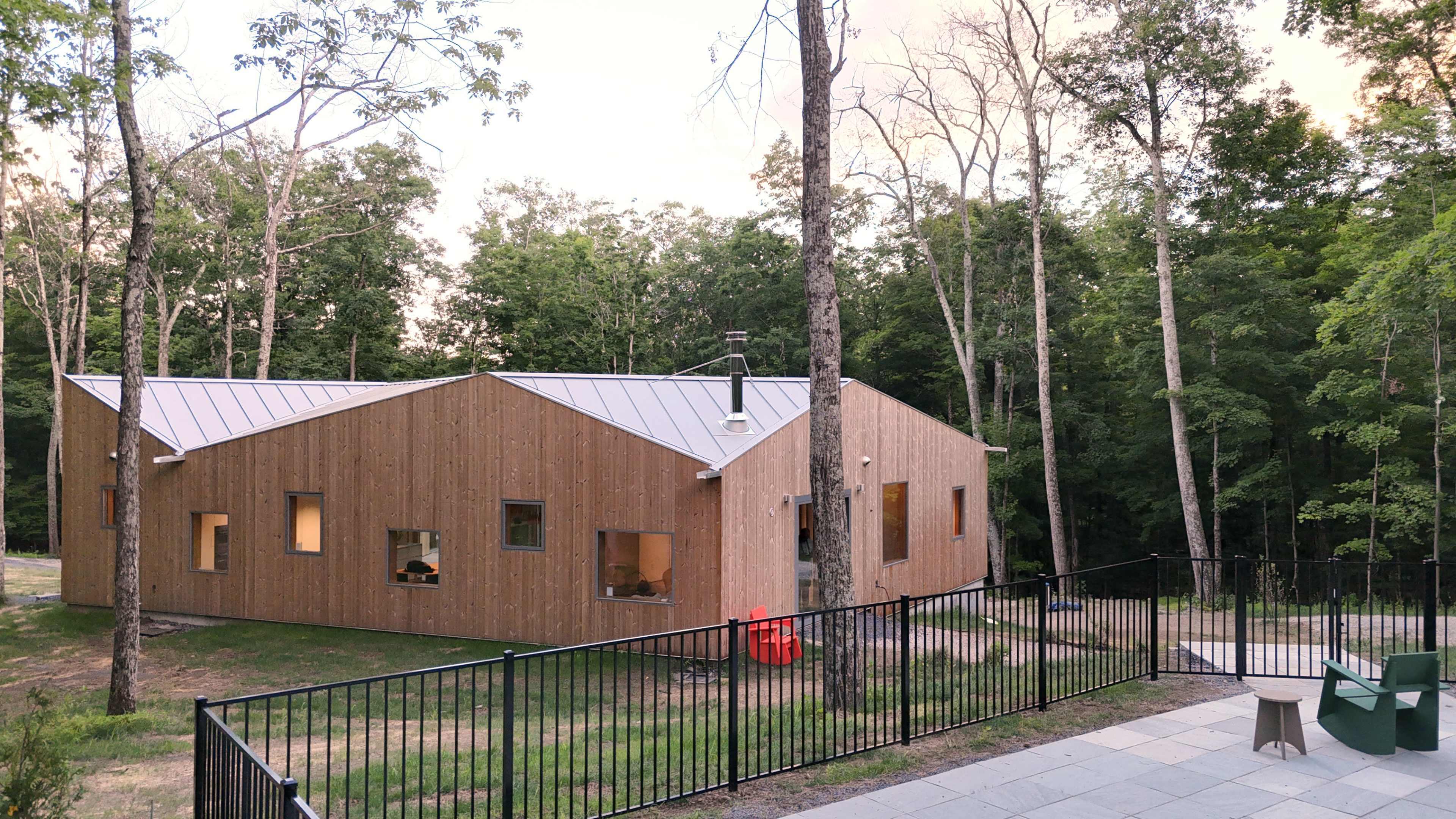 A modern wooden house with a slanted roof is situated among trees in a green forested area.