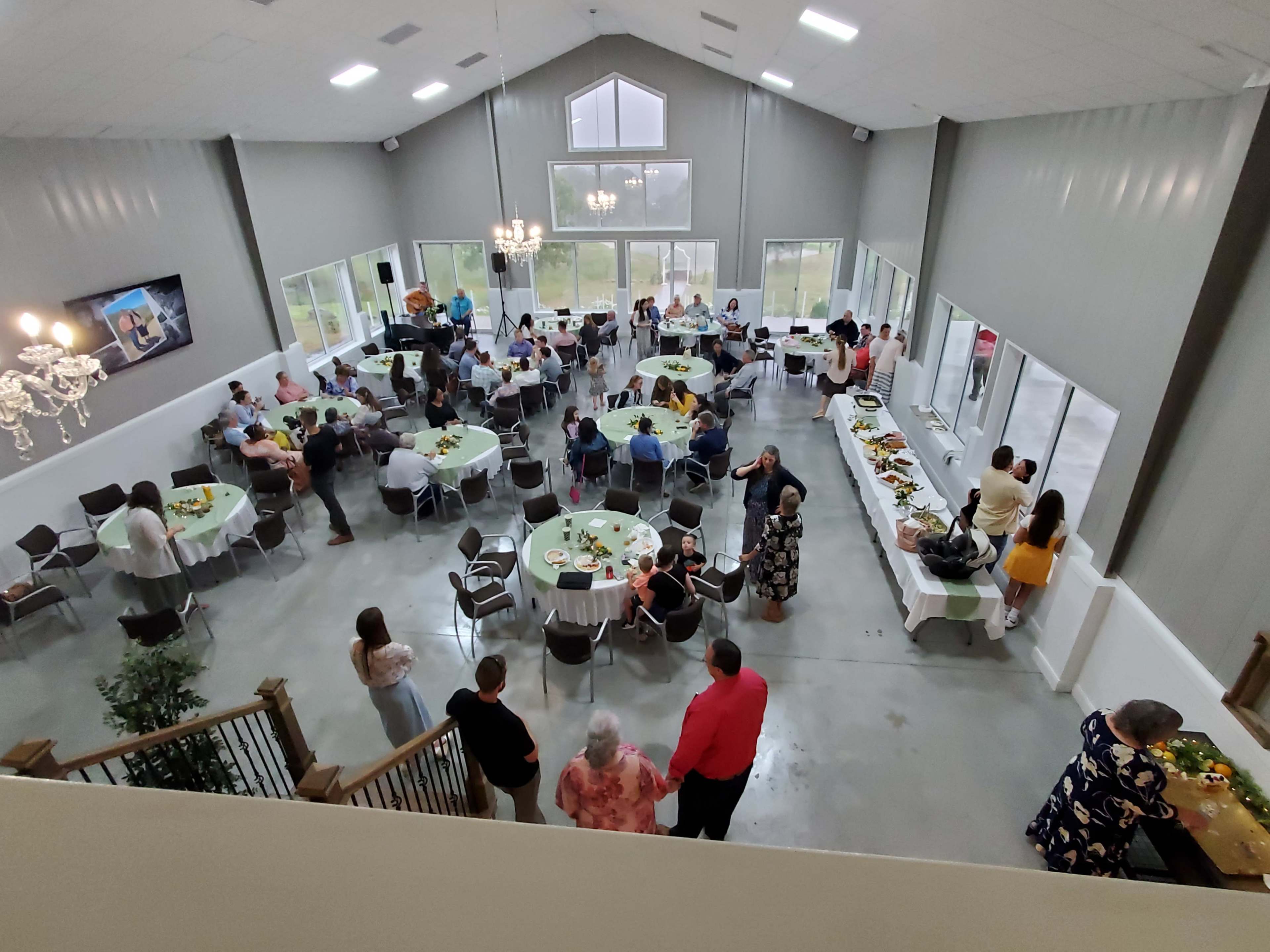 A gathering is taking place in a spacious indoor venue with tables set for dining and guests mingling around a buffet.