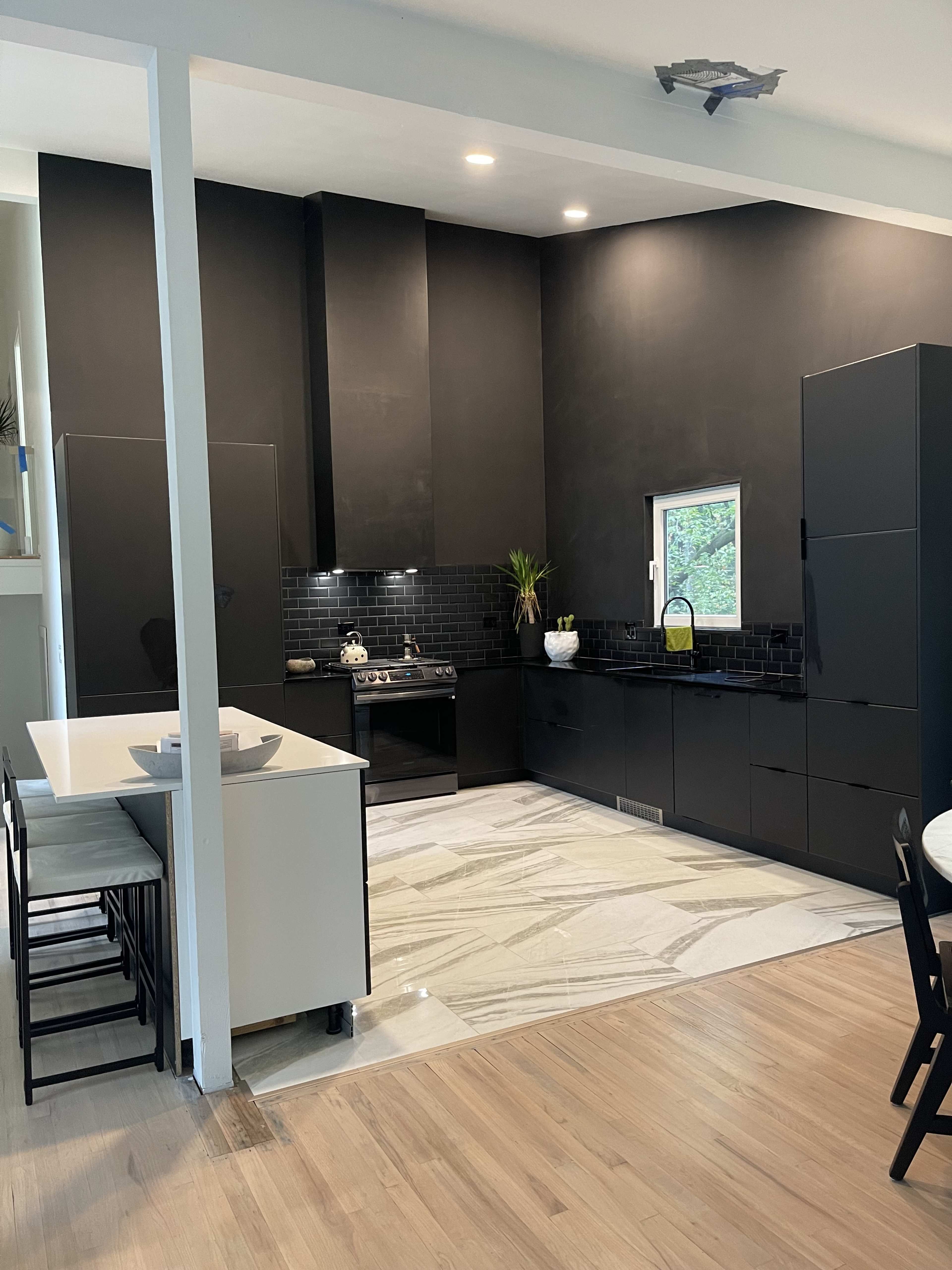 A modern kitchen with black cabinetry, a gas stove, and marble flooring.