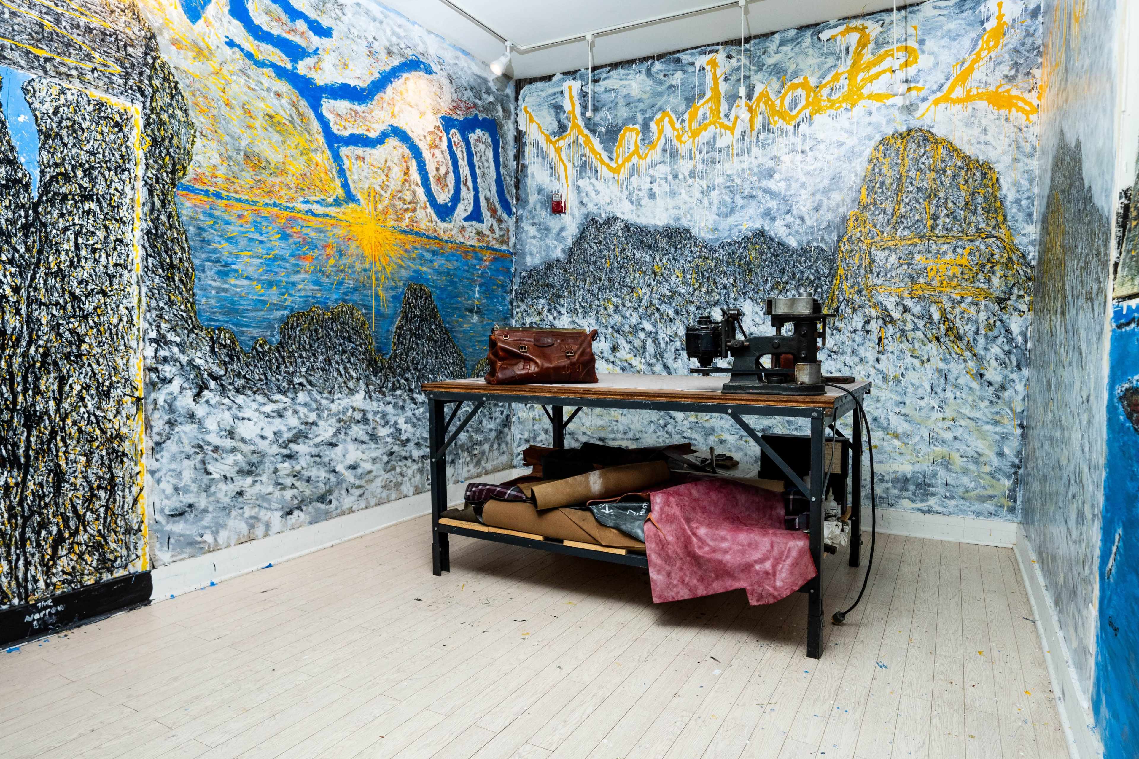 An interior room with abstract murals on the walls, a table with a sewing machine, and assorted materials stacked underneath.