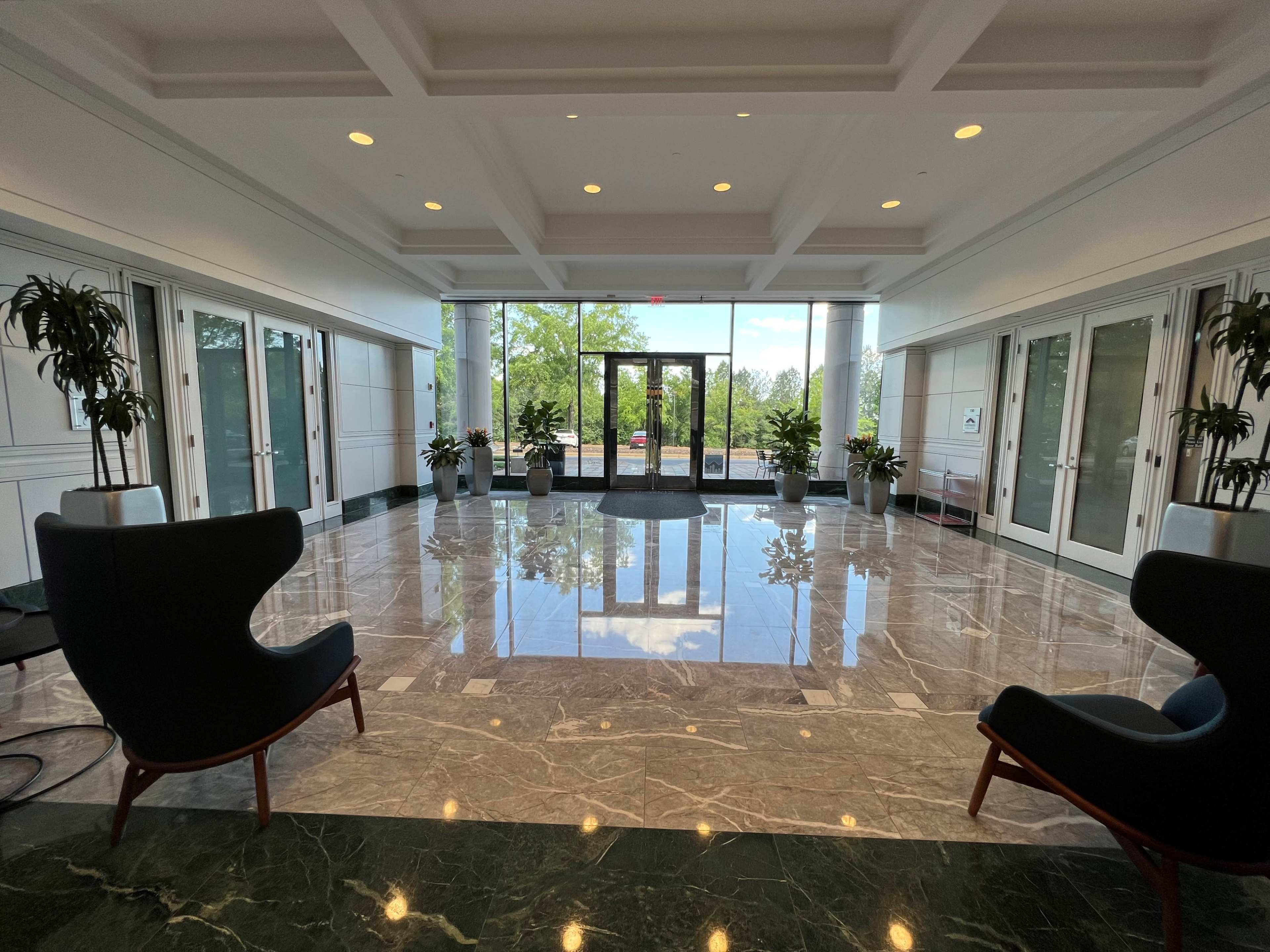 A spacious lobby with marble flooring, two black chairs, and large glass doors leading to an outdoor area.
