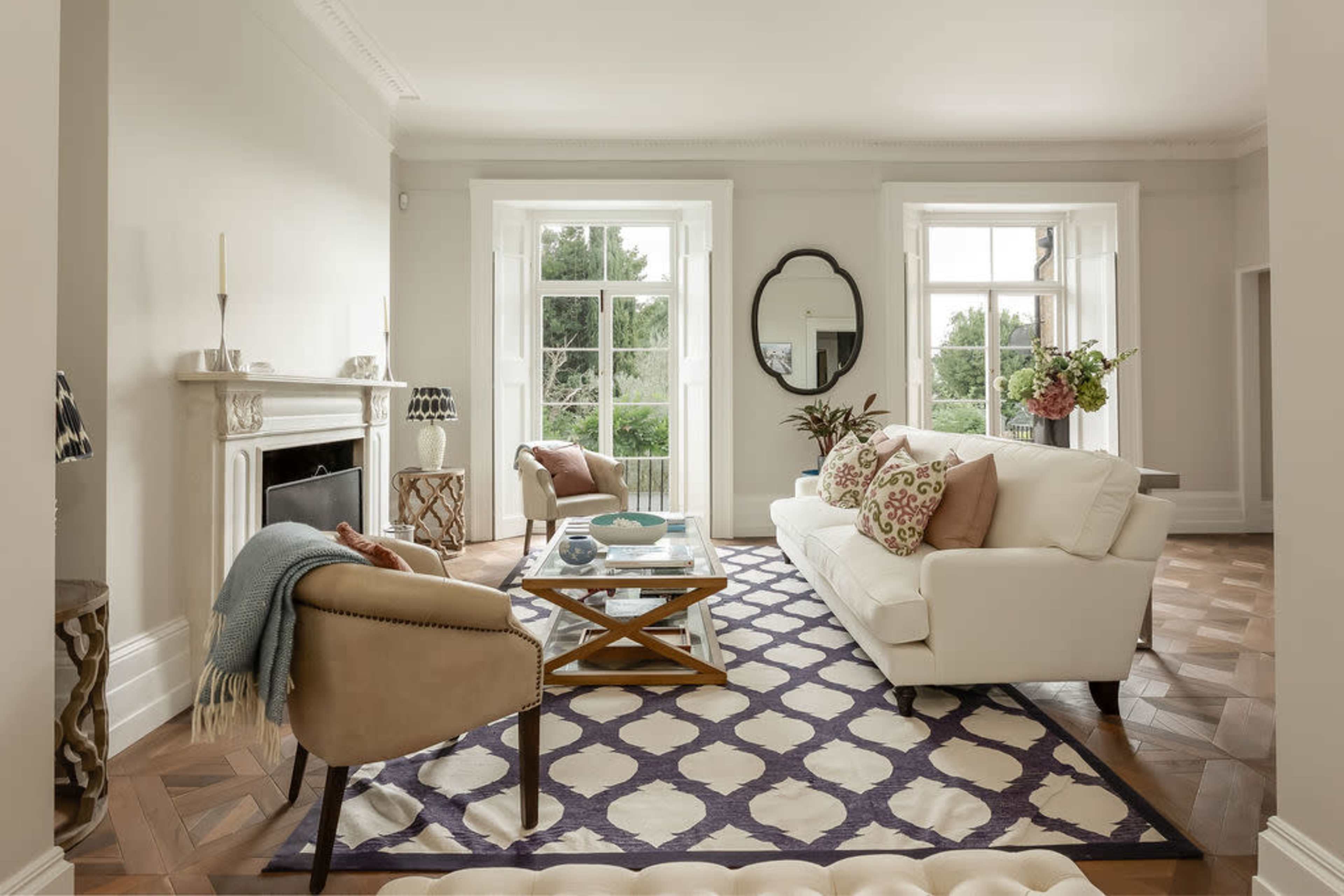 The image shows a modern living room featuring a white sofa, a glass coffee table, and large windows allowing natural light to fill the space.