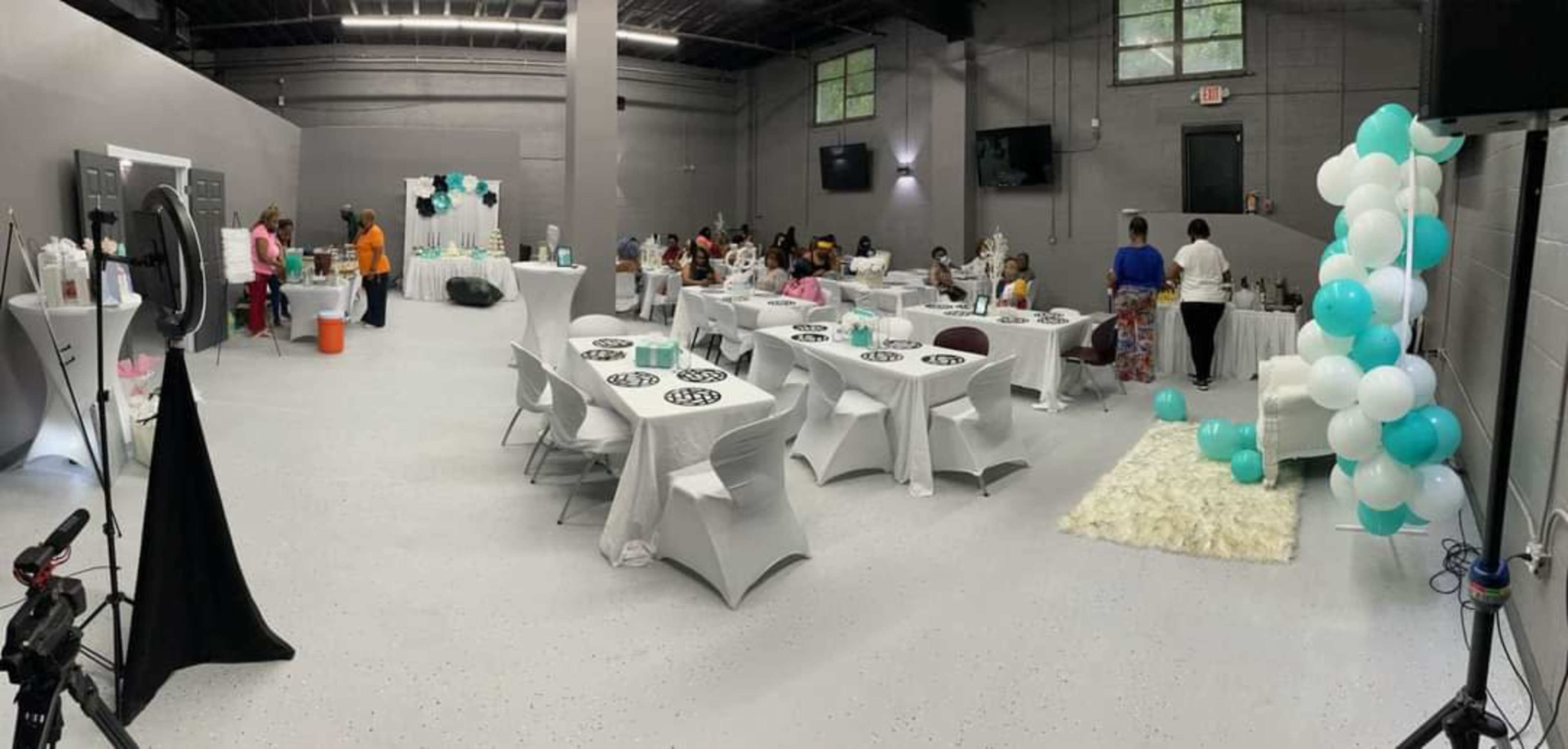 An indoor event space with neatly arranged tables, decorations in teal and white, and guests seated throughout the area.