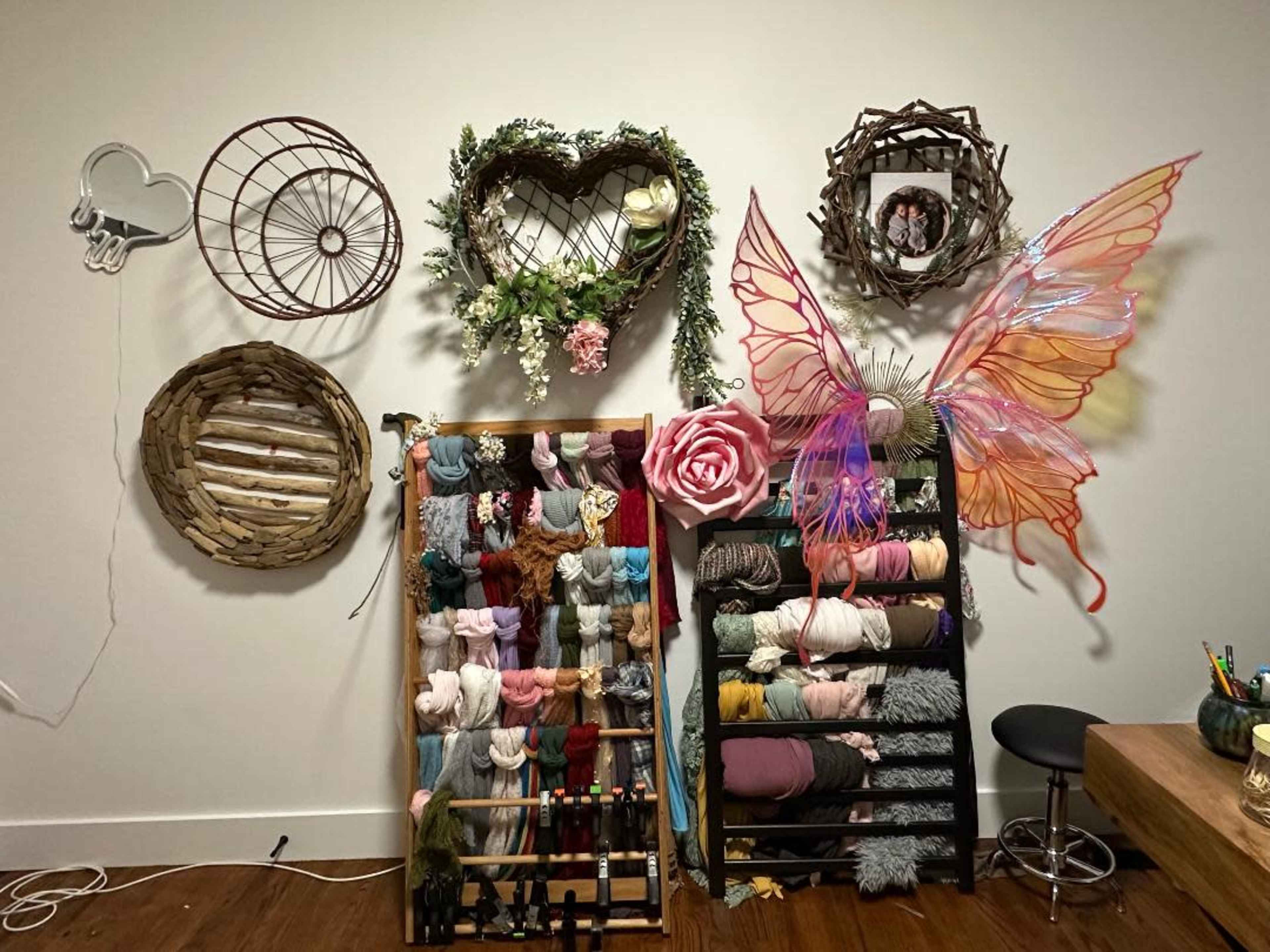 A light-colored wall decorated with various woven wall hangings, a floral arrangement, and a large, colorful butterfly piece, alongside a yarn organizer filled with different shades of yarn.