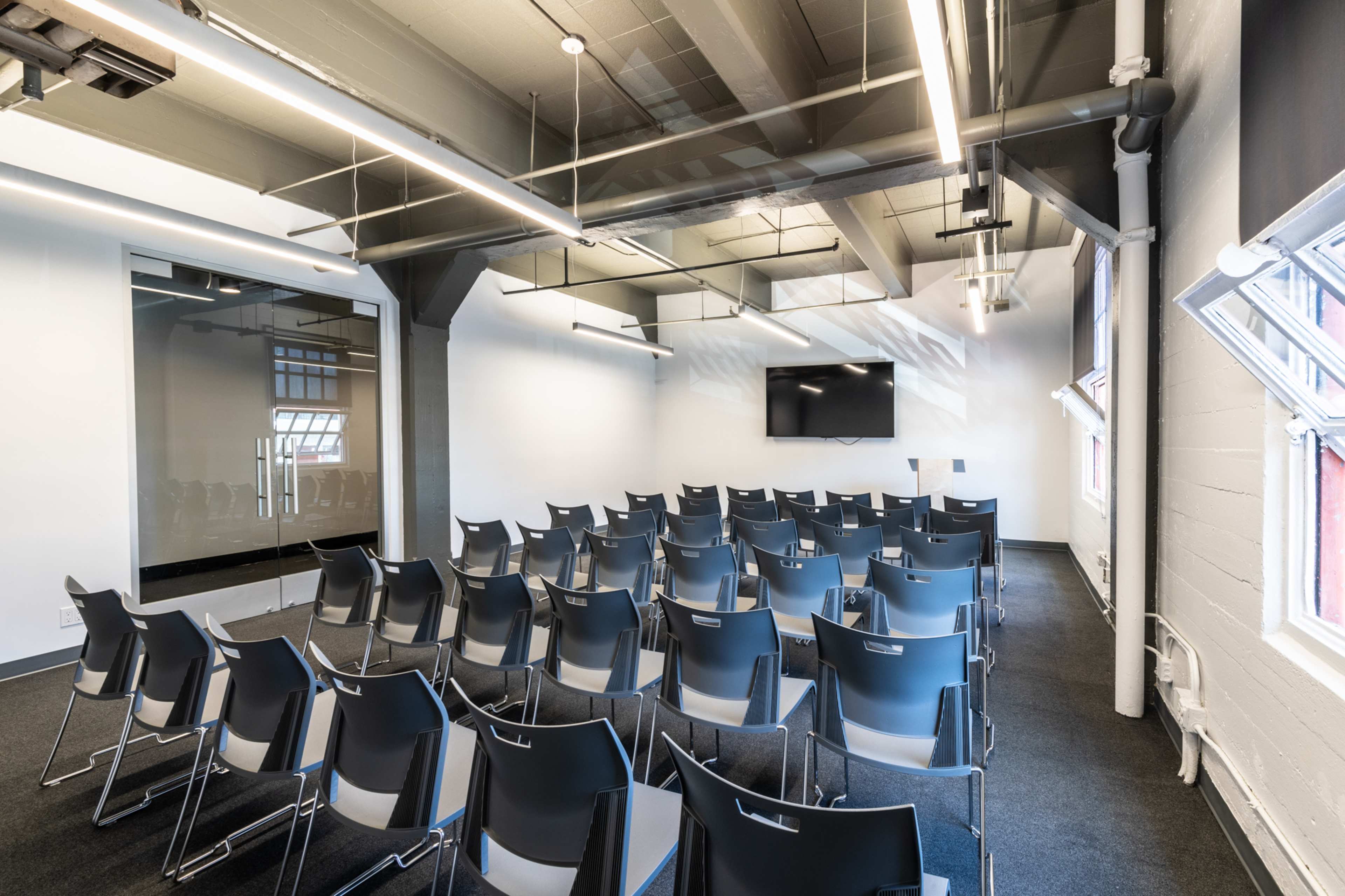 A modern conference room set up with rows of black chairs facing a wall-mounted screen.
