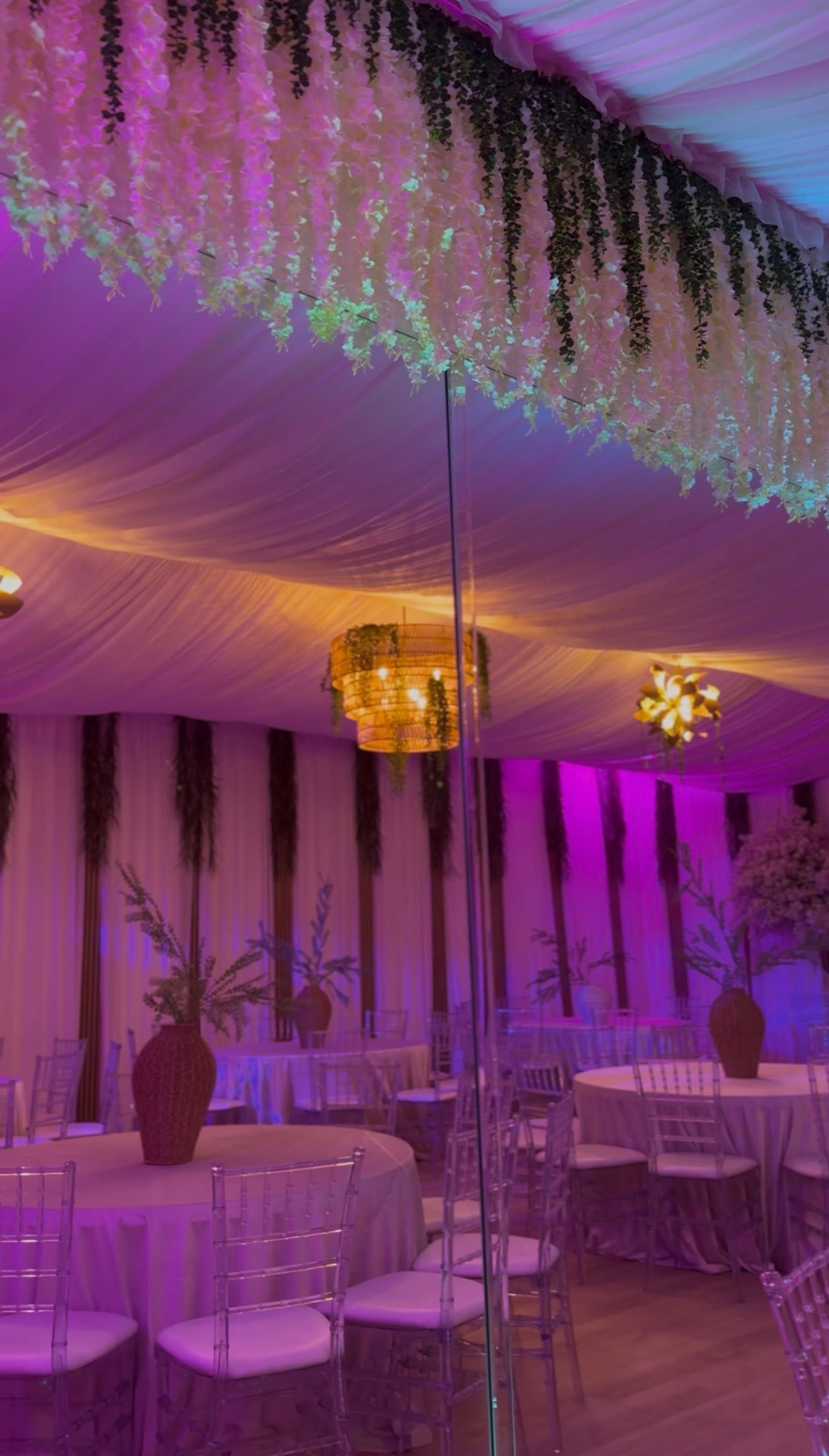 The image shows an elegantly decorated indoor event space with draped fabric, chandeliers, and floral arrangements.