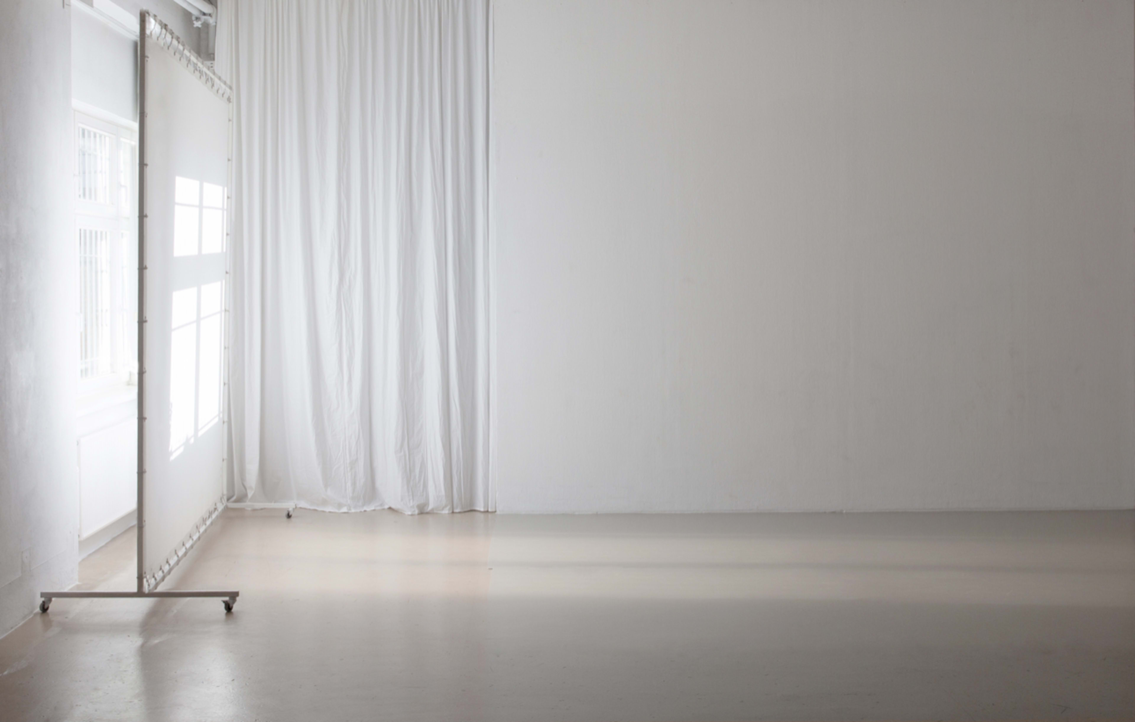 A minimalist room features a large white curtain and a partition with windows, set against a light-colored floor.