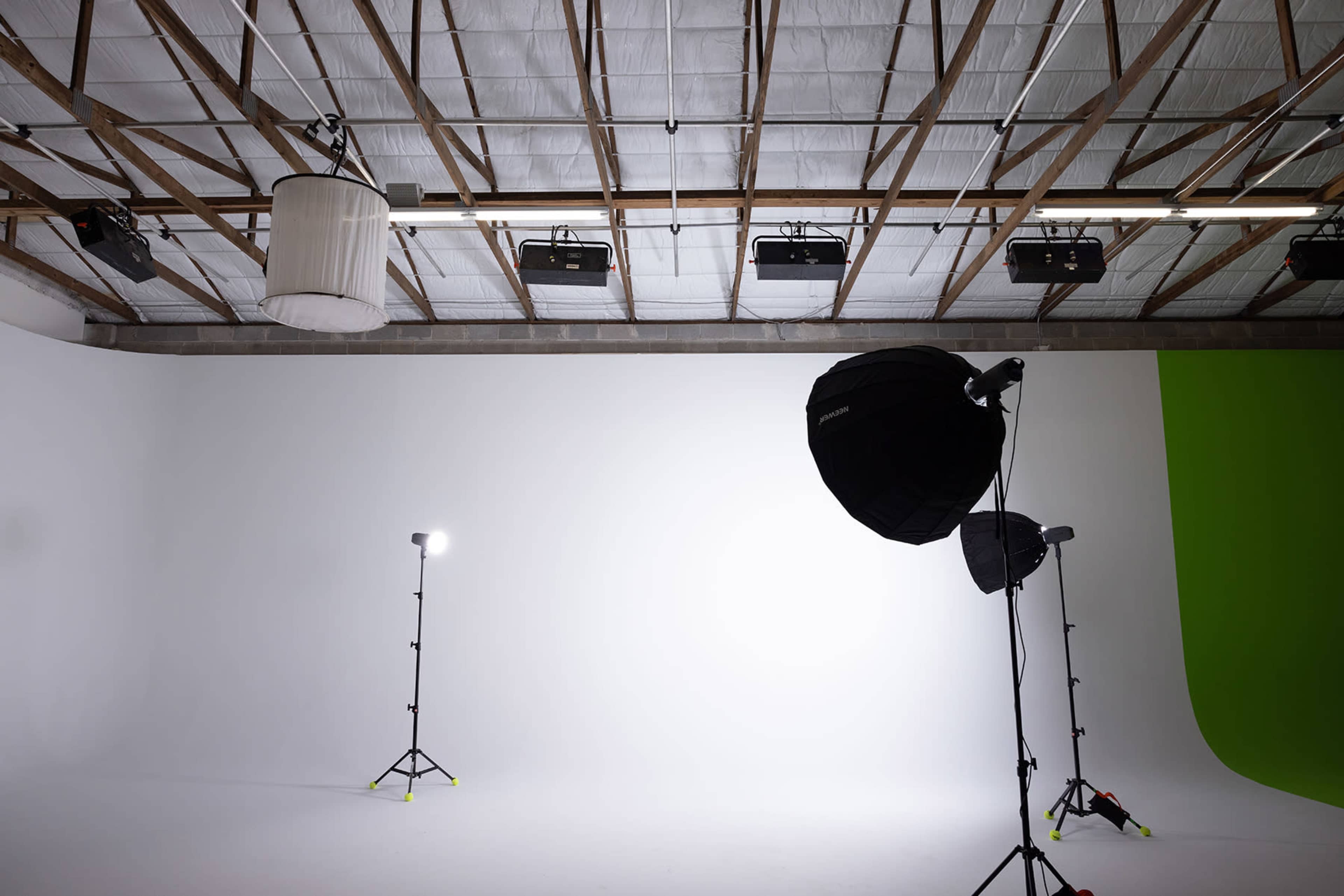 The image shows a minimalist studio setup featuring a white backdrop, softbox lights on stands, and a green screen in the corner.