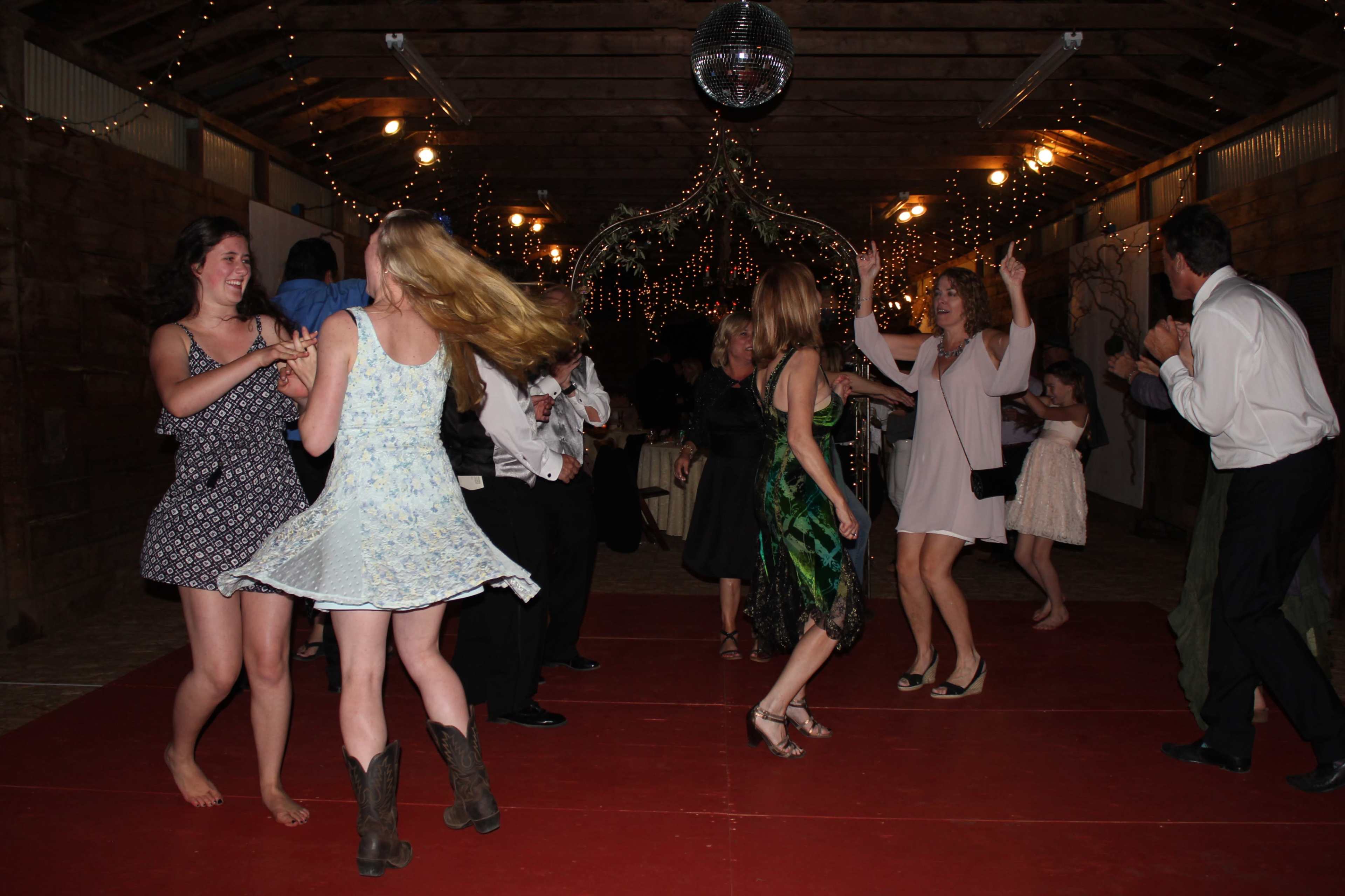 A group of people dances on a red floor under twinkling lights in a decorated indoor venue.