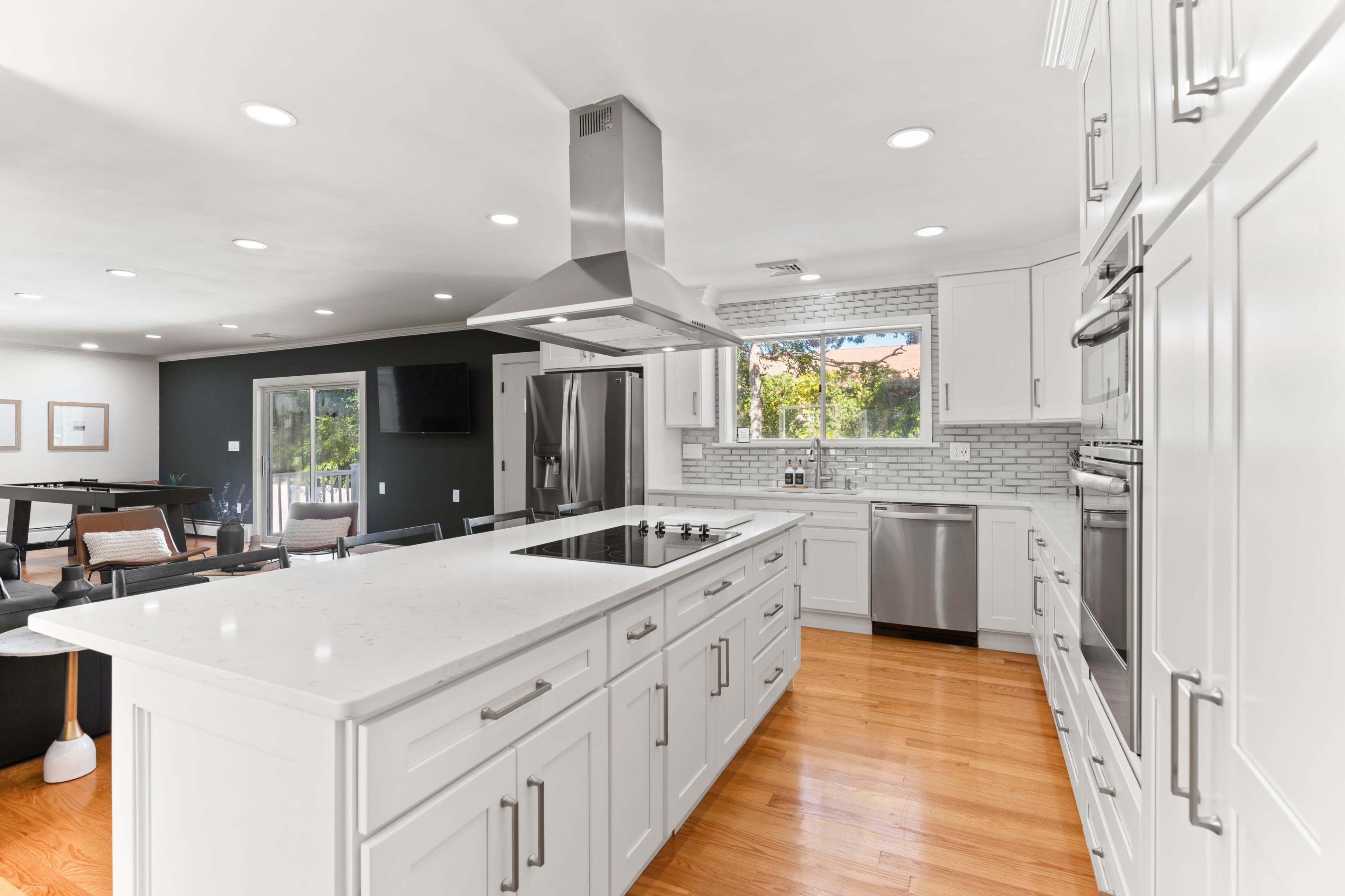 A modern kitchen features white cabinetry, a central island with a cooktop, and stainless steel appliances, with a window providing natural light.