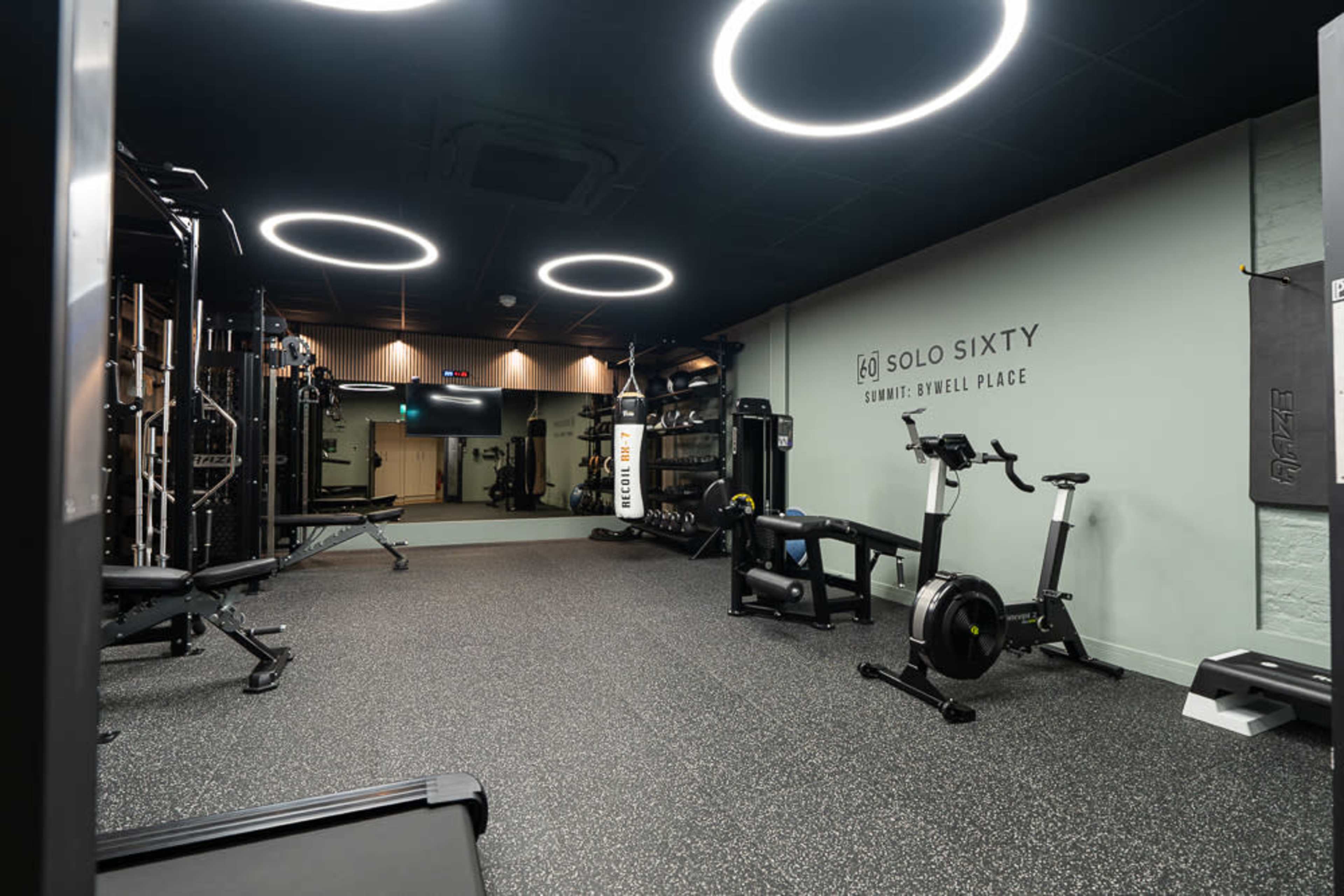 The image shows a modern gym interior with various workout equipment and circular LED lighting on the ceiling.