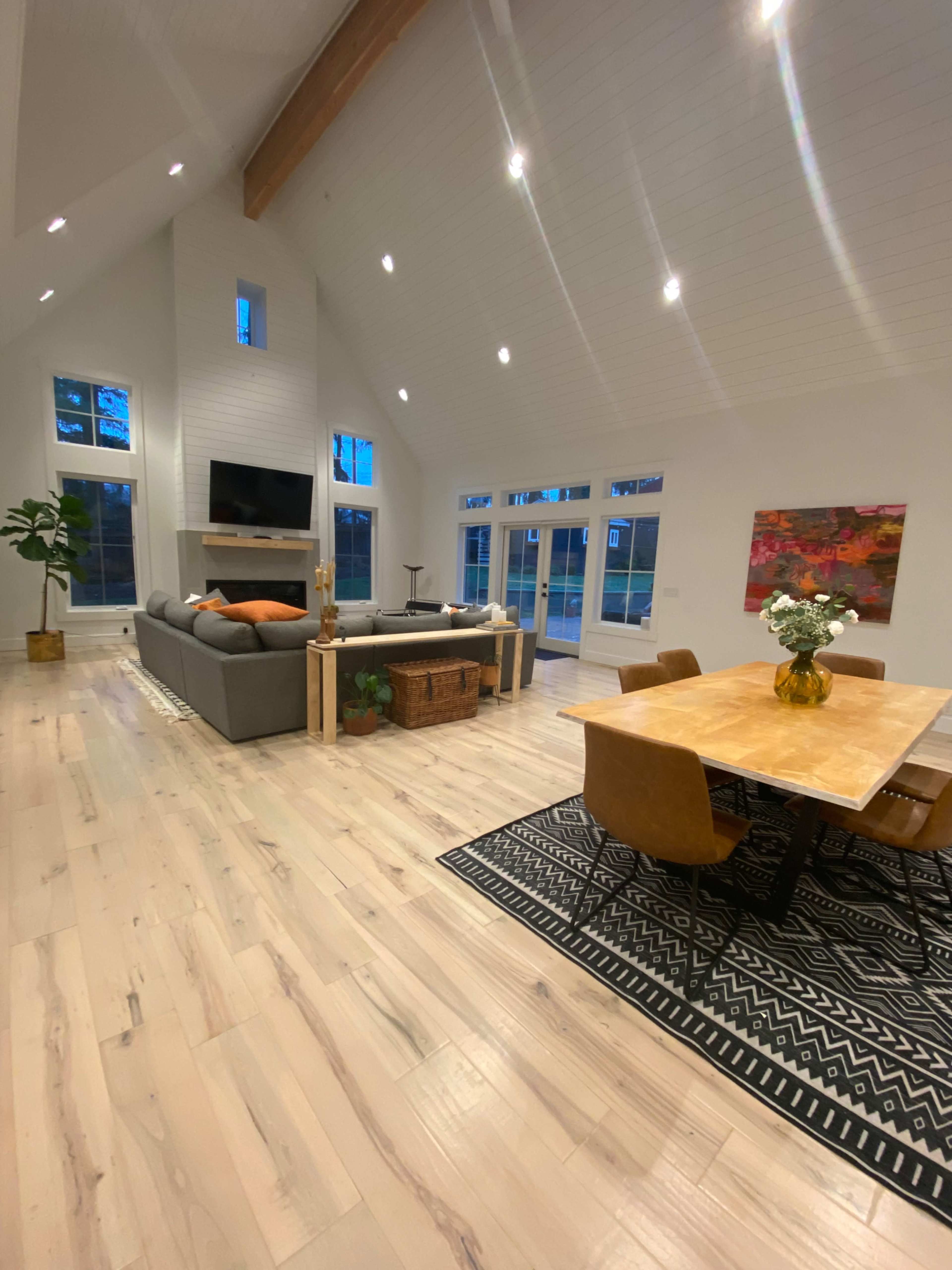 The image shows a spacious modern living area with a couch, dining table, and large windows allowing natural light to fill the room.