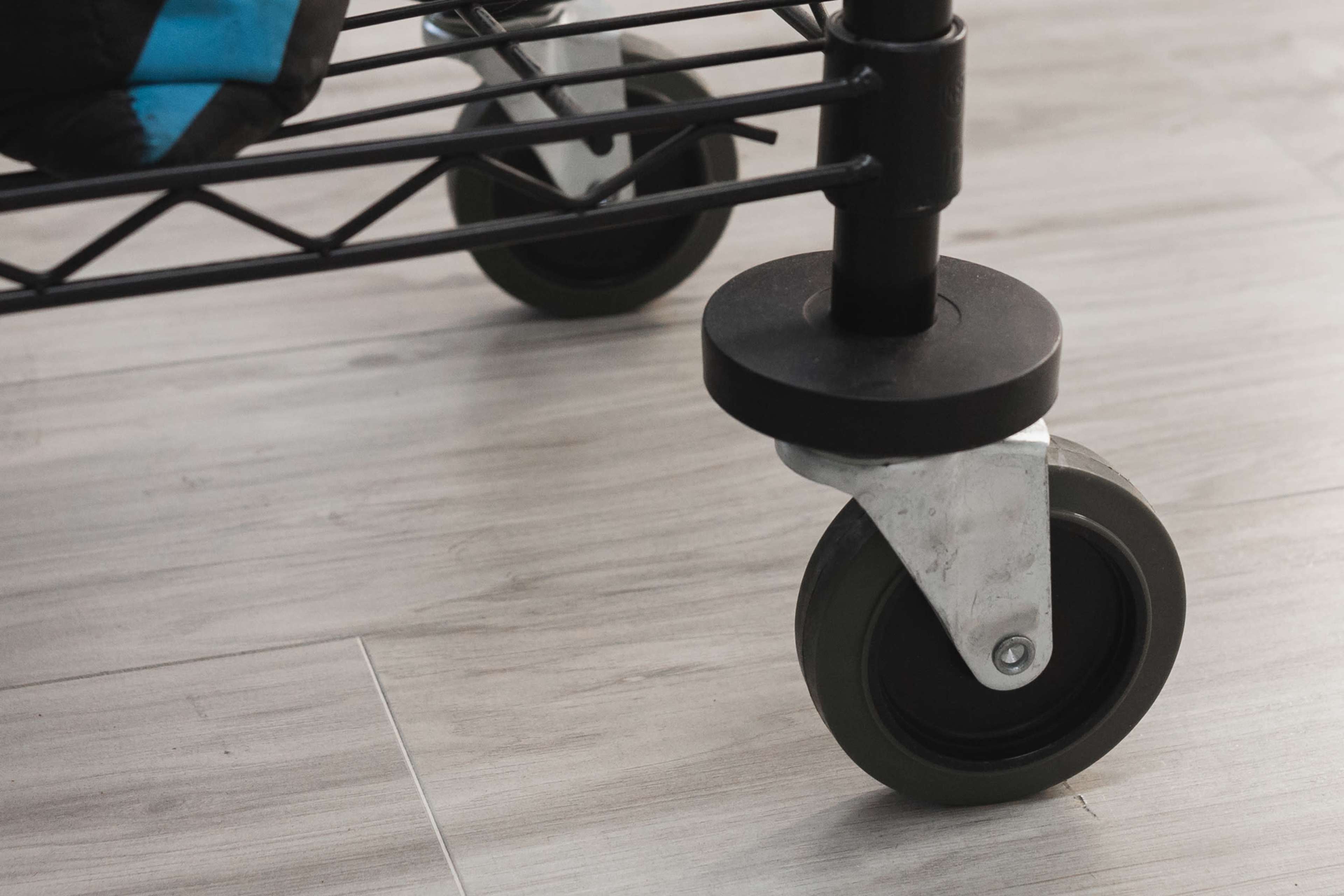 A close-up of a metal cart's wheel resting on a wooden floor.