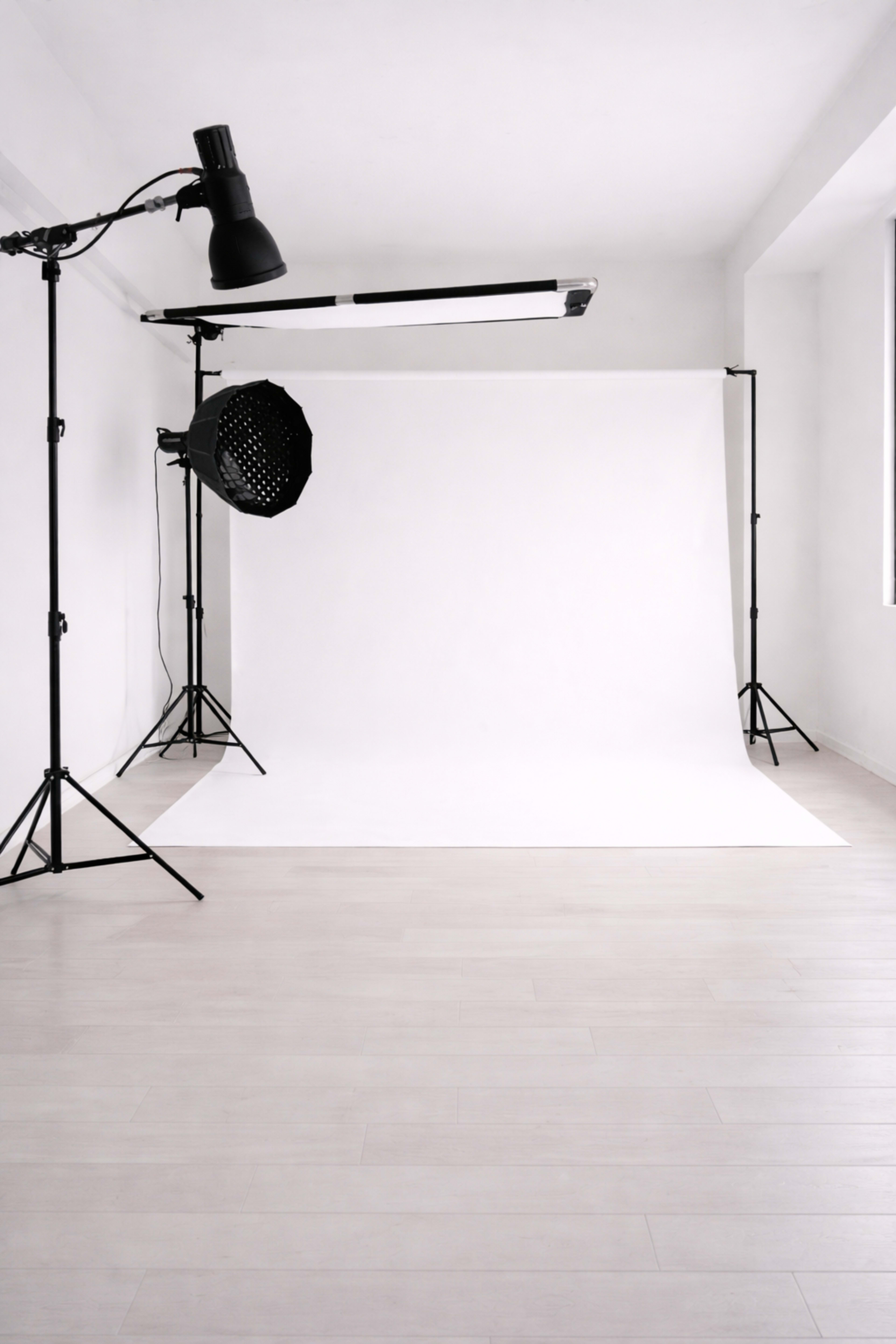 The image shows a photography studio with a white backdrop and studio lighting equipment set up on either side.