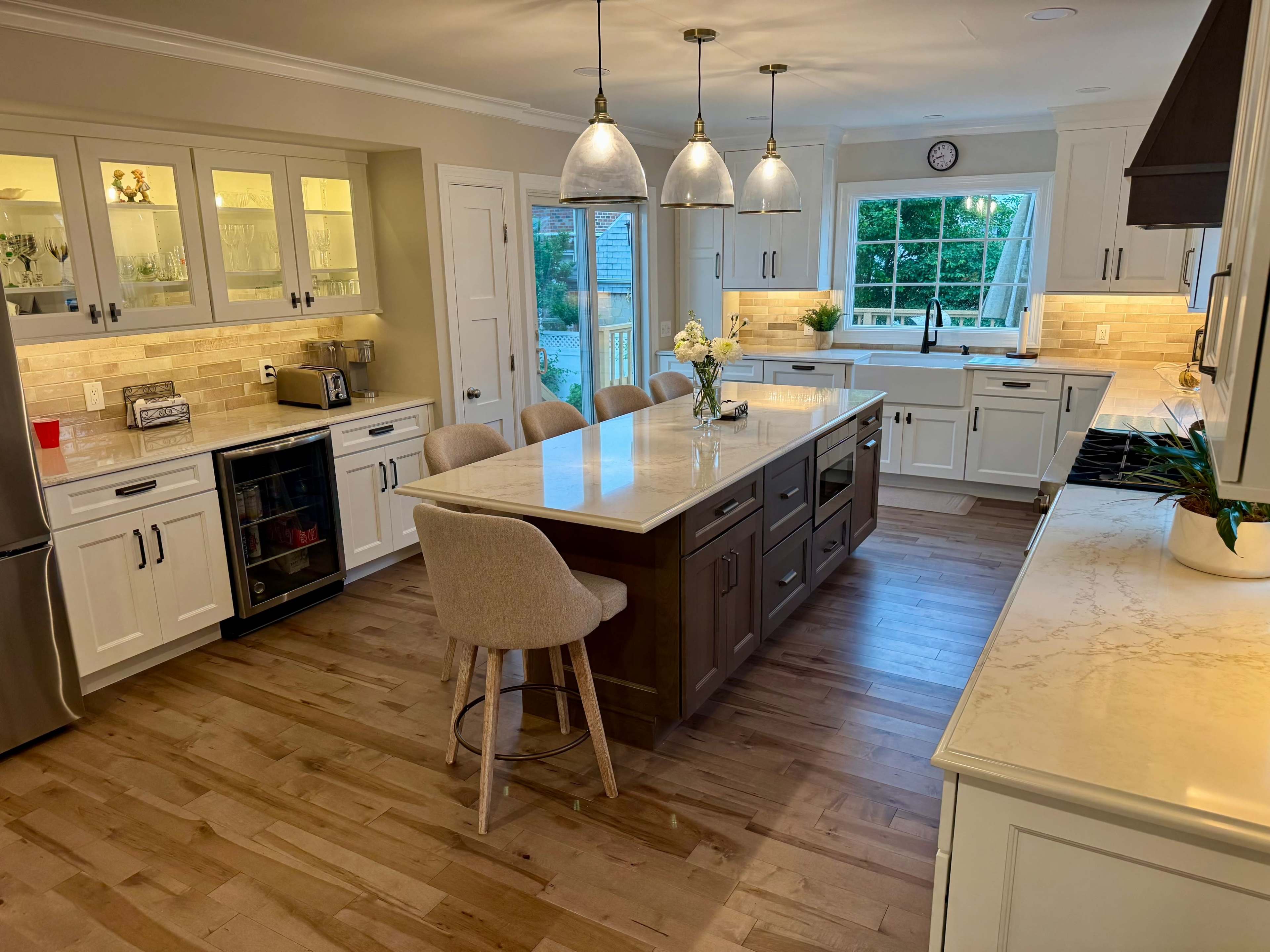 The image shows a modern kitchen with white cabinetry, an island with a dark wood base, and pendant lighting above.