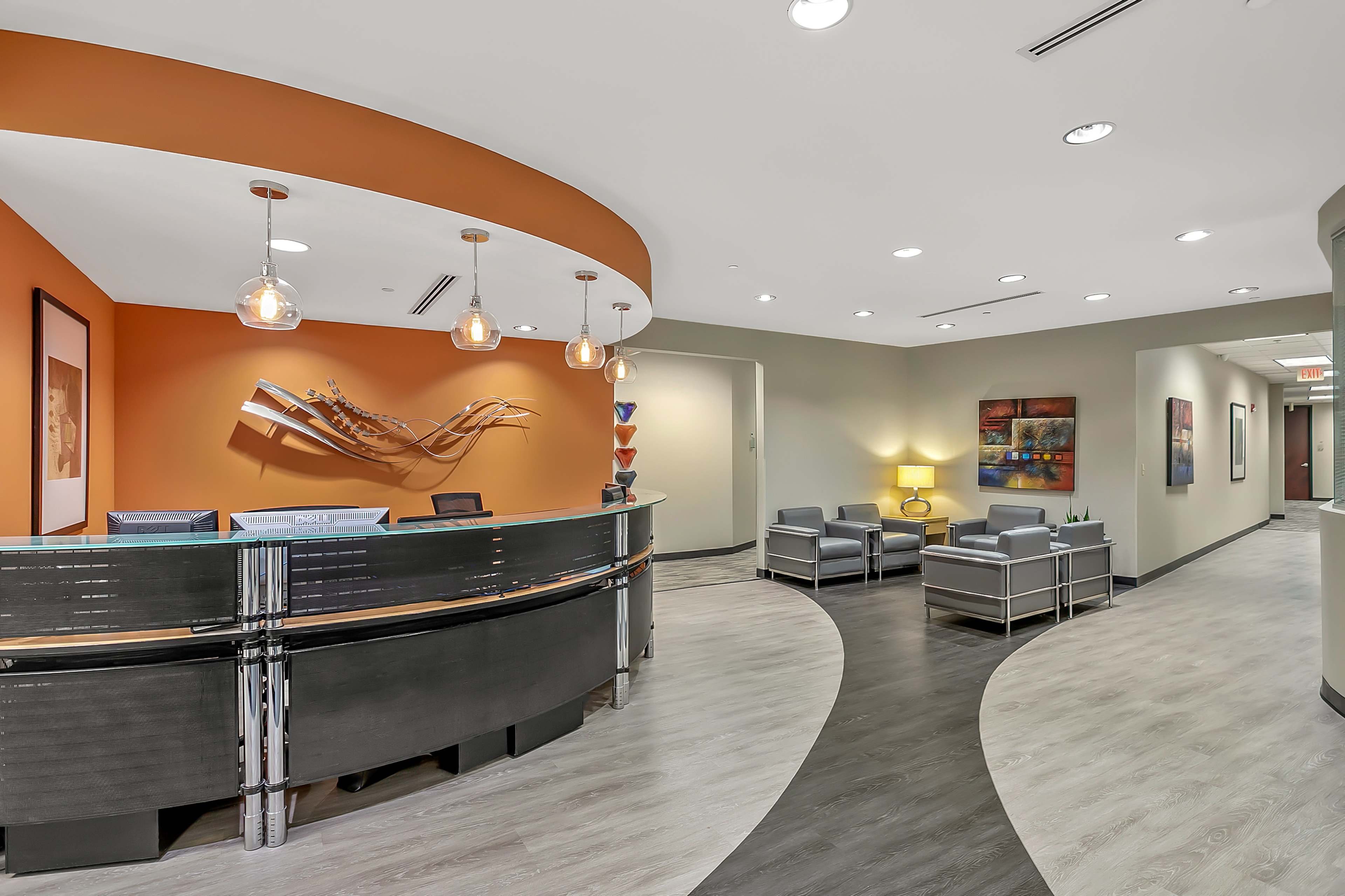 The image shows a modern reception area featuring a curved desk, contemporary seating, and decorative wall art in a well-lit setting.