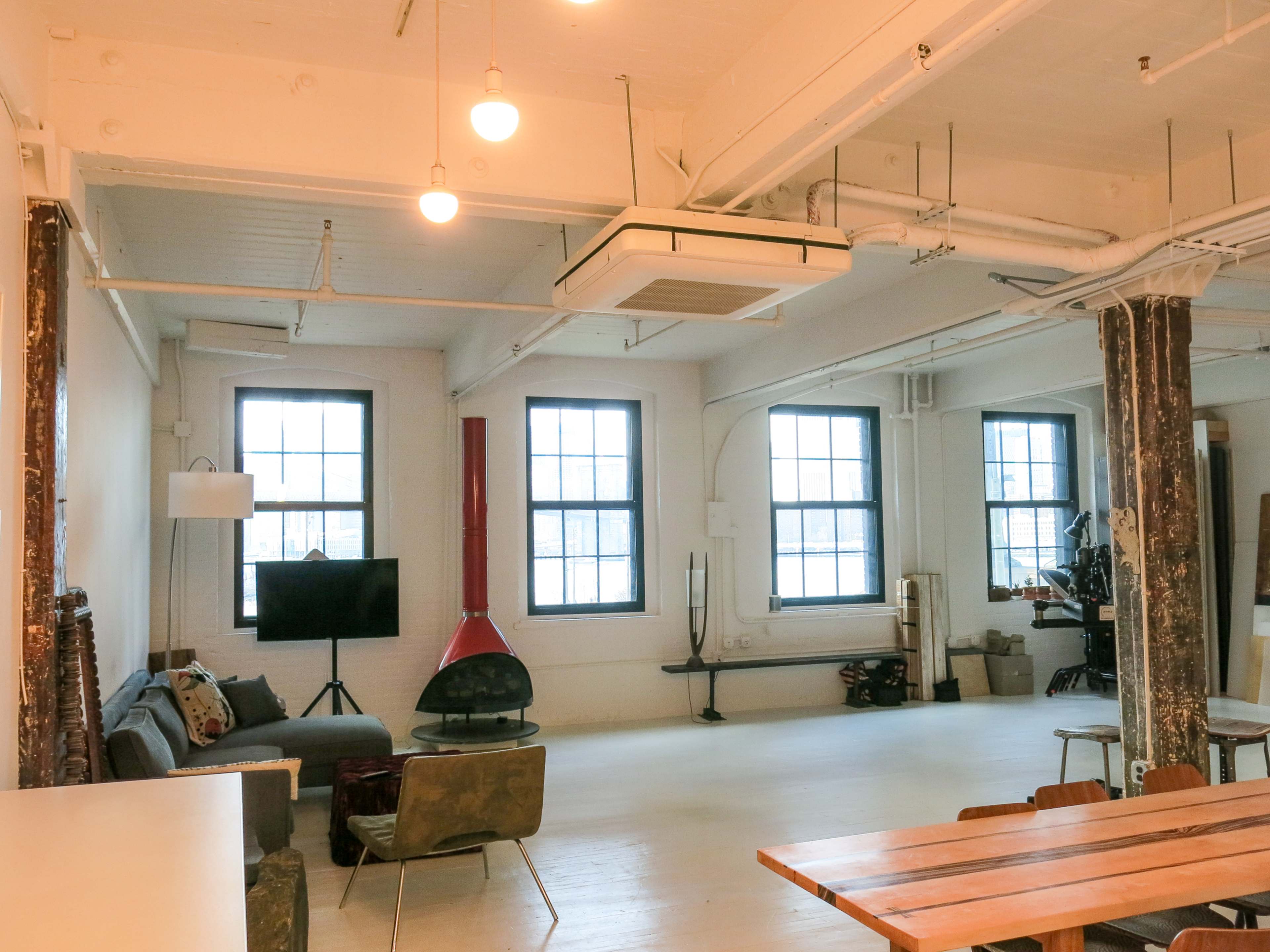A spacious, modern living area with large windows, a low couch, a television, and a central dining table made of wood.
