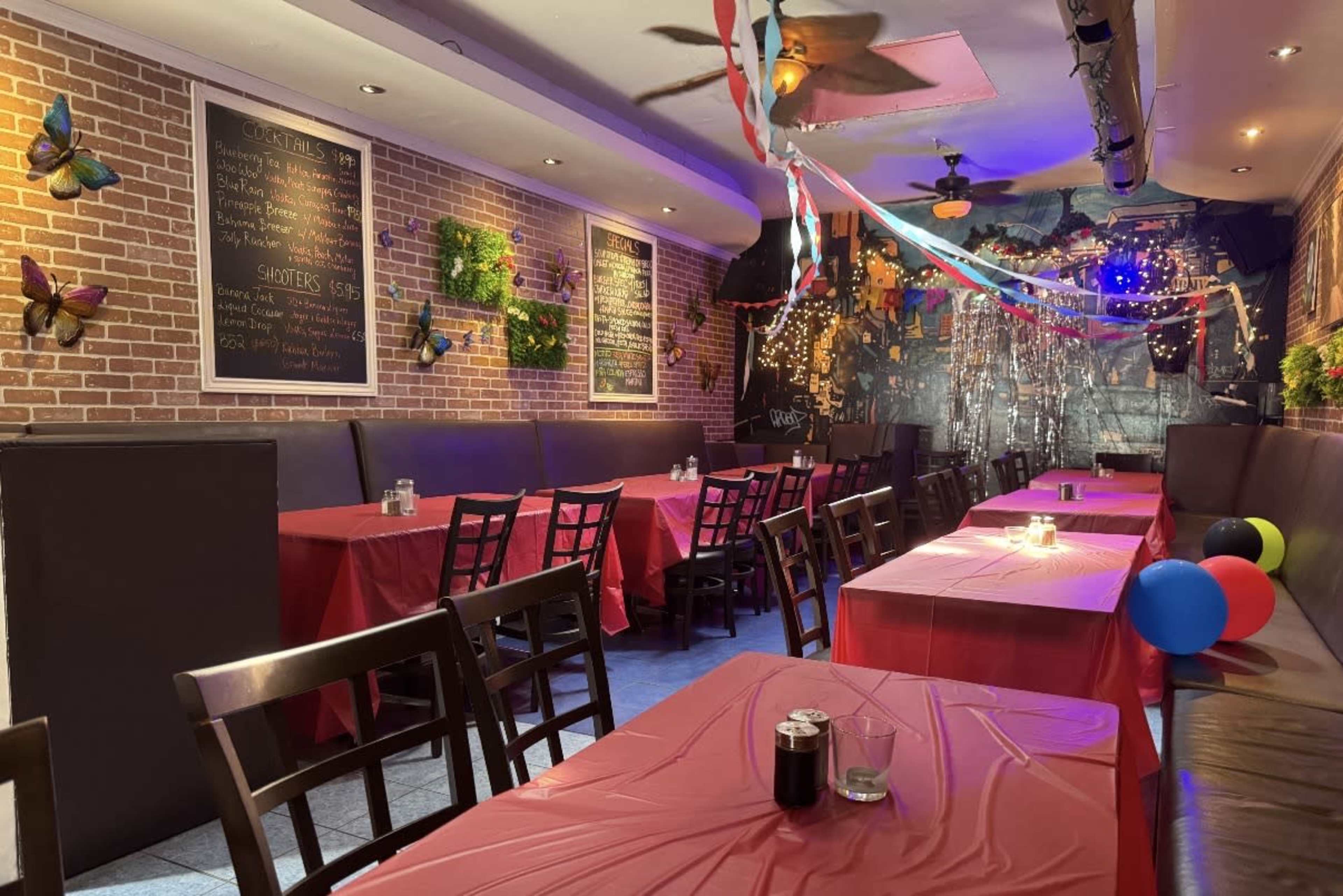 The image shows an event space with red tablecloths on tables, dark wooden chairs, and decorative elements like butterflies and streamers hanging from the ceiling.