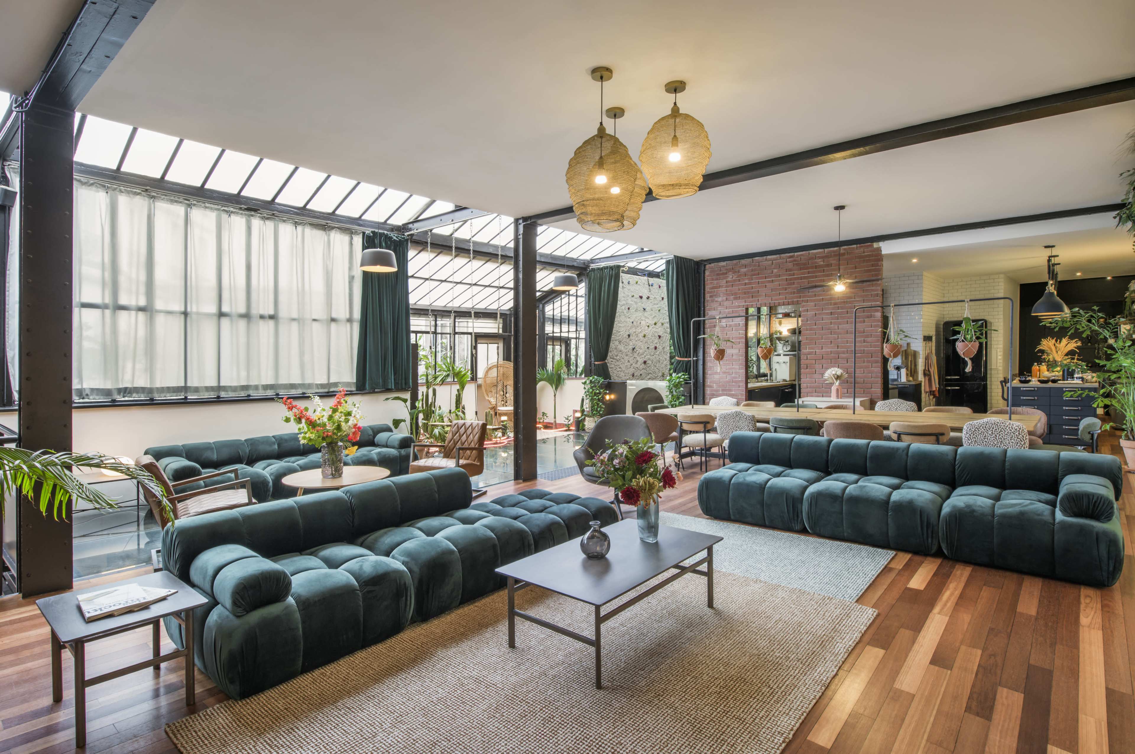 The image shows a modern living space with two large teal sofas, a central coffee table, and large windows allowing natural light to fill the room.