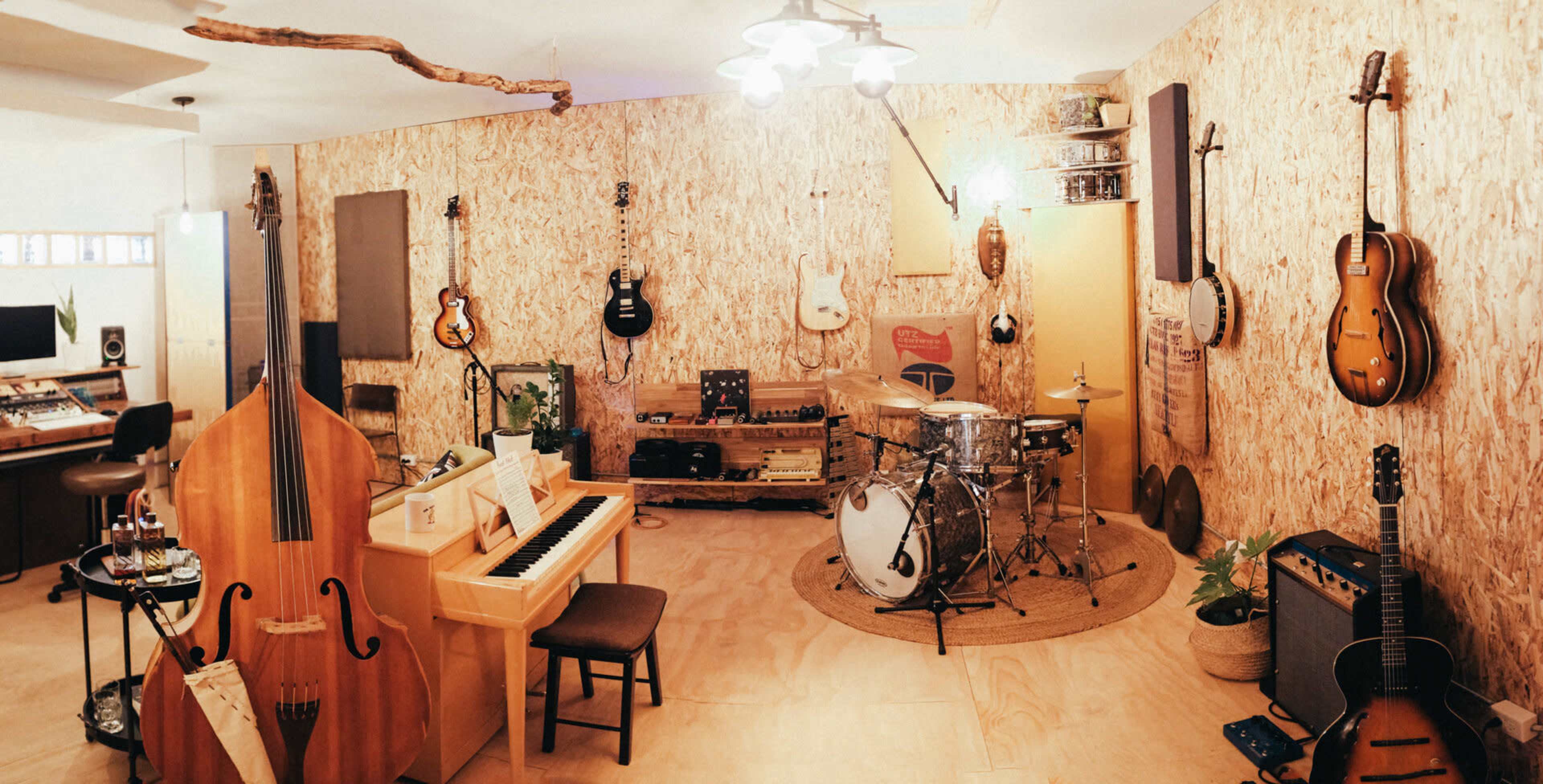 The image depicts a music rehearsal space with various instruments, including guitars, a drum set, and a piano, arranged against wooden walls.