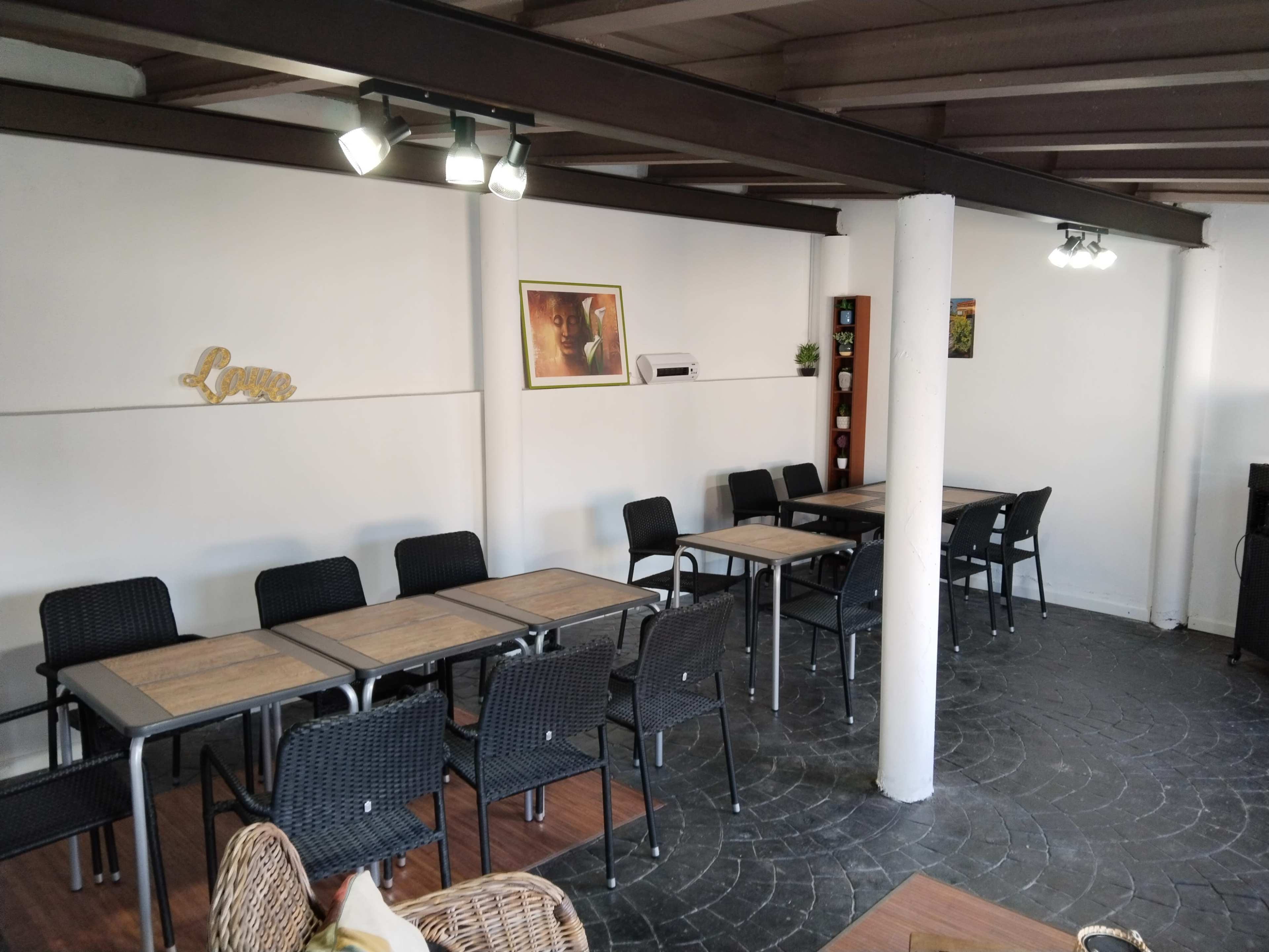 The image shows a spacious indoor seating area with several wooden tables and black chairs arranged neatly under a beam ceiling.