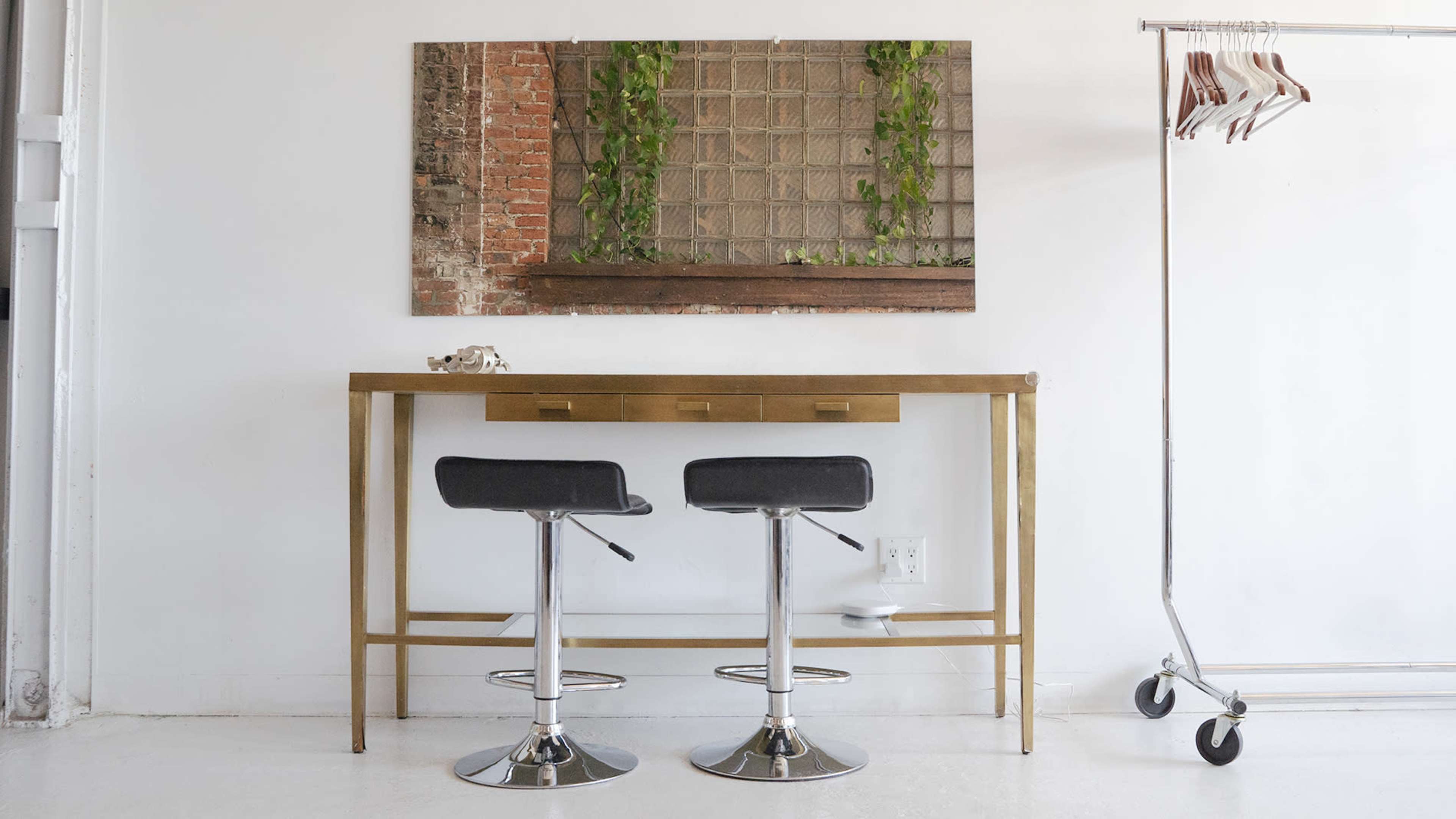 A modern entryway with two black bar stools positioned at a gold console table, reflected in a large wall-mounted mirror adorned with greenery.