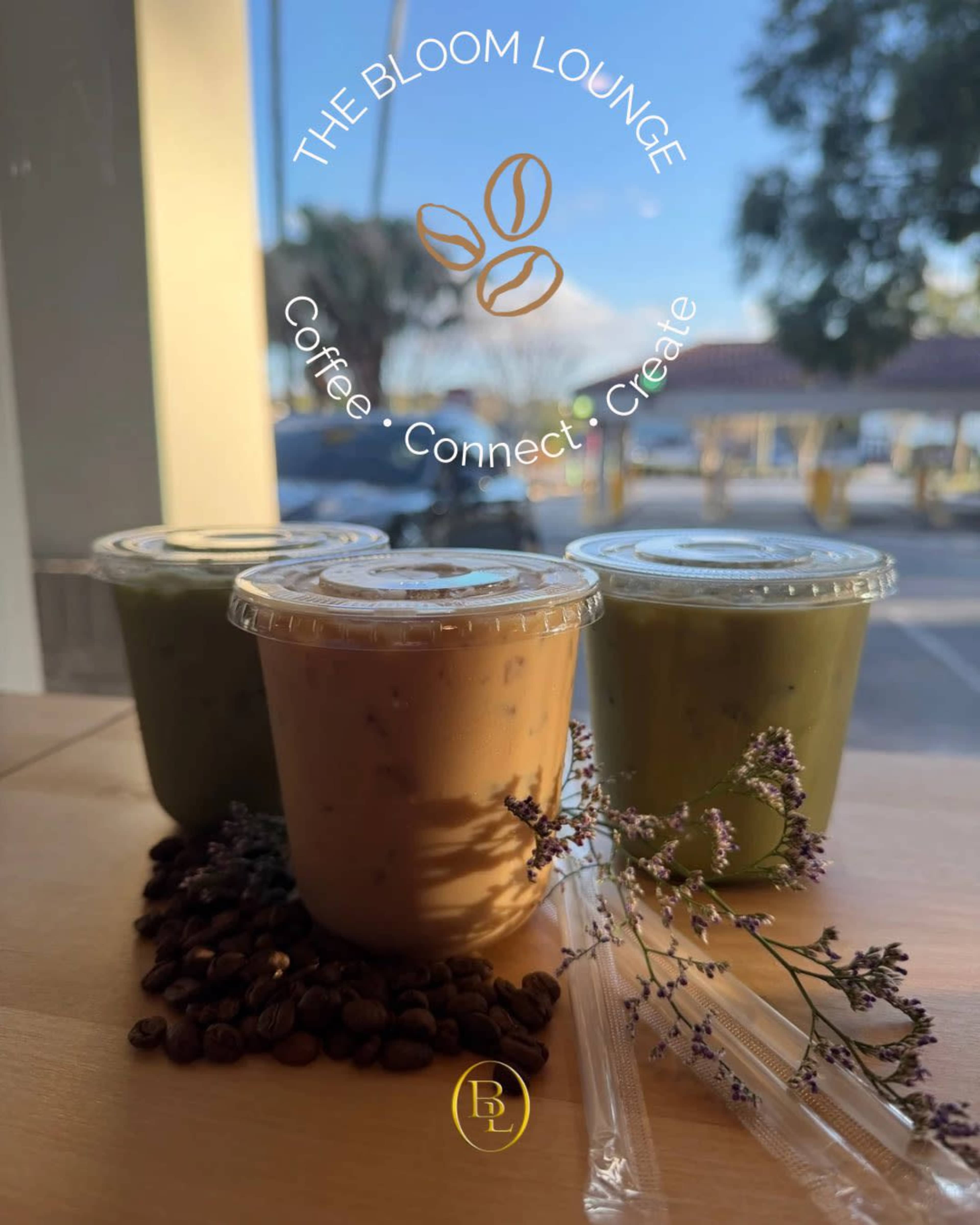 The image shows three cups of iced beverages on a wooden surface, surrounded by coffee beans and small flowers, with a blue sky visible through a window.