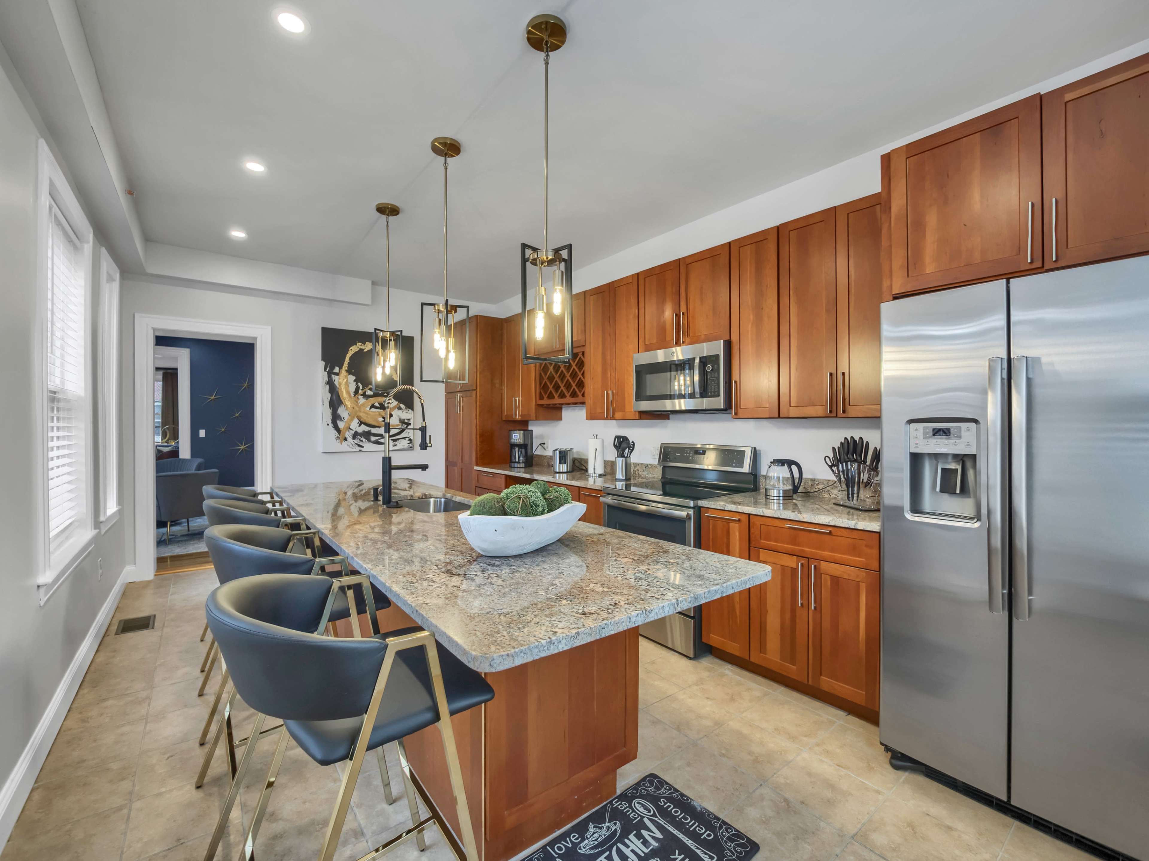 A modern kitchen features dark wood cabinetry, stainless steel appliances, and a central island with bar stools and pendant lighting.
