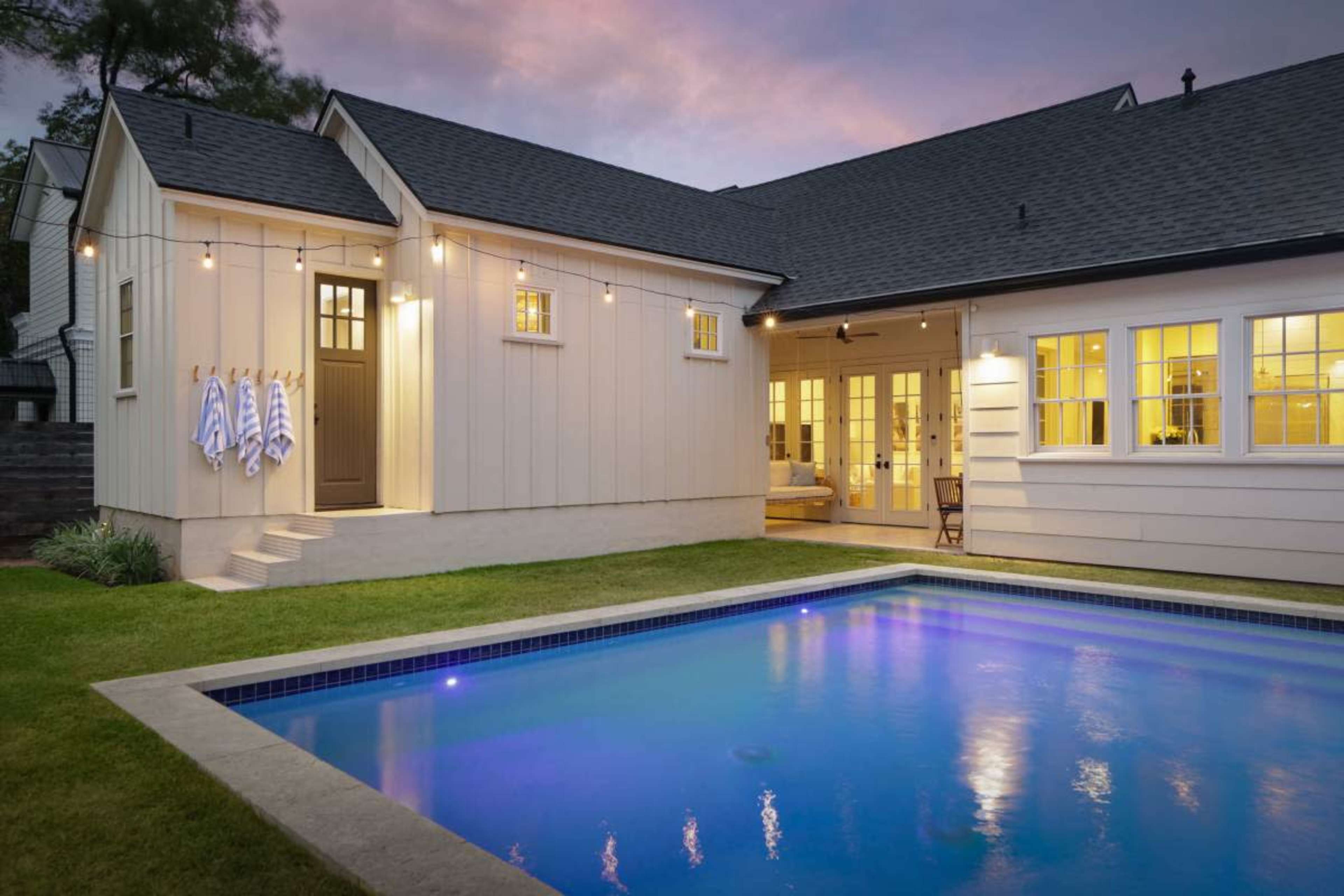 A modern house with a swimming pool in the backyard features a patio and several towels hanging by the entrance.