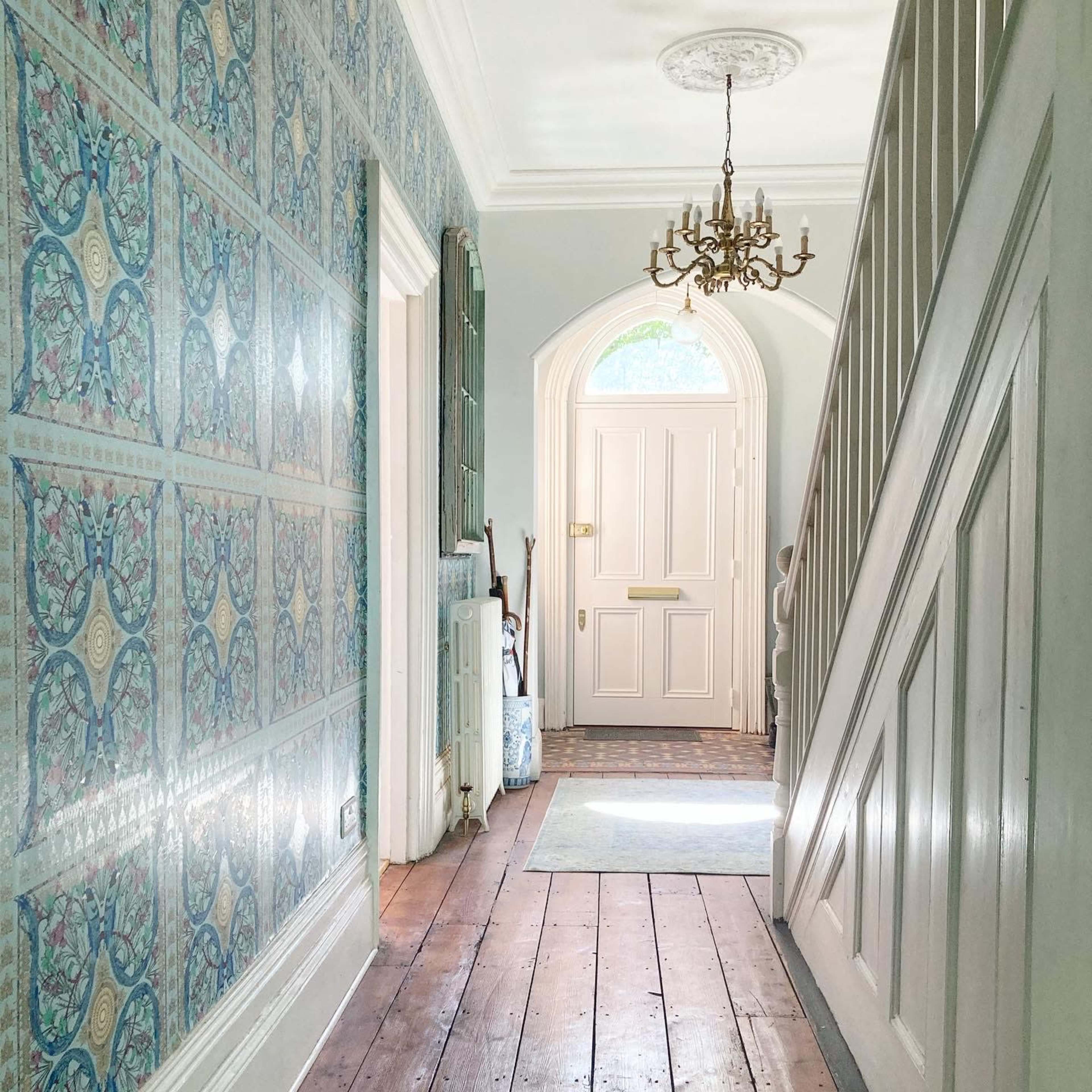 A hallway features patterned wallpaper, a staircase on the right, and a door at the far end leading outside.
