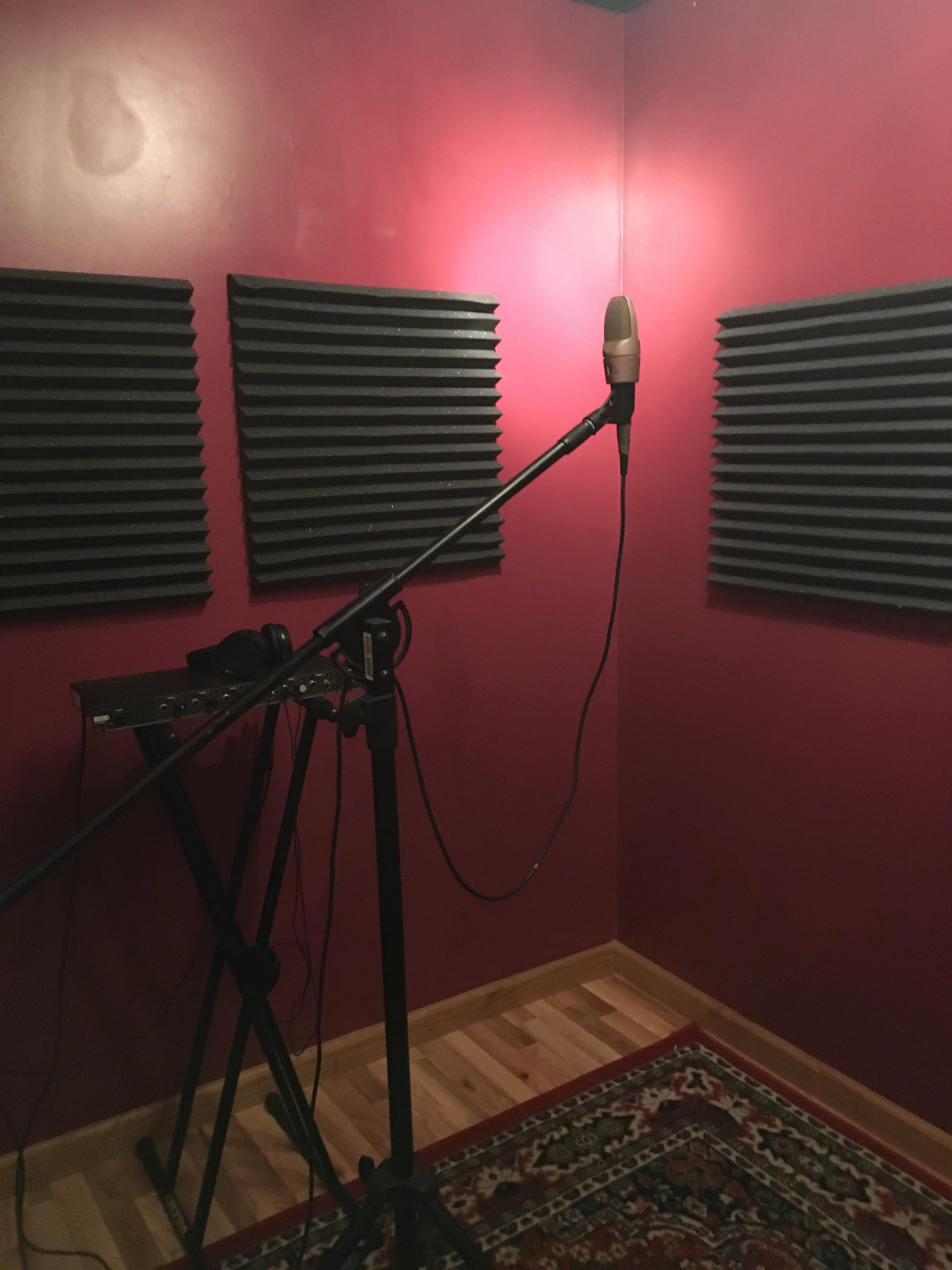 A small recording studio with a microphone on a stand, black soundproofing panels on the walls, and a keyboard on a stand.