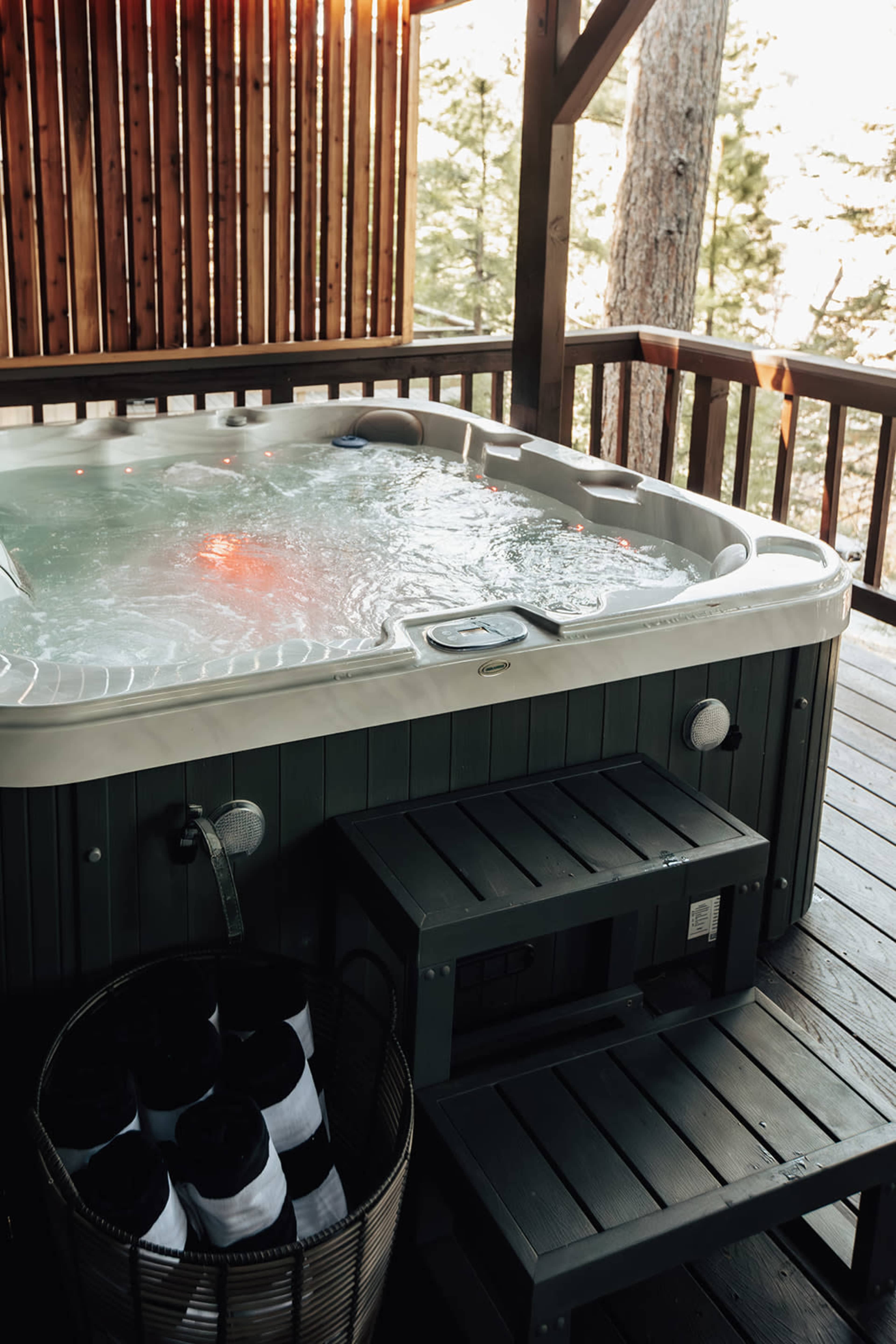 A hot tub with bubbling water is situated on a wooden deck surrounded by trees.