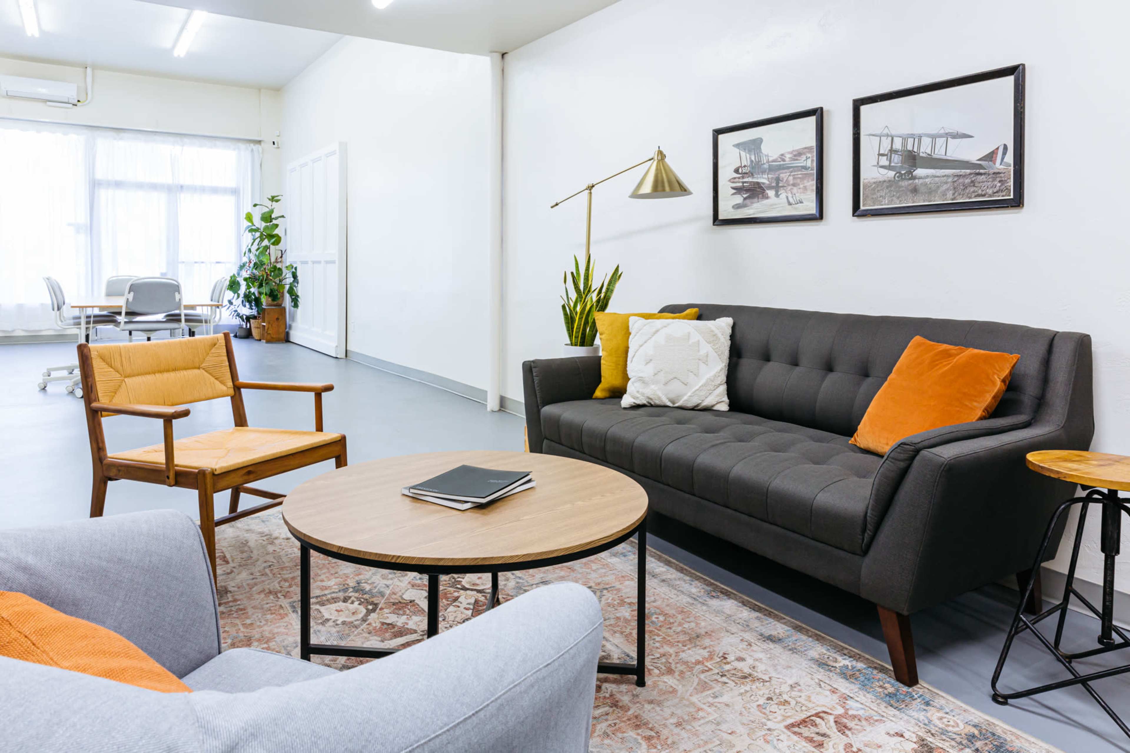 A modern sitting area with a gray couch, an orange-accented chair, a round coffee table, and framed artworks on the wall.
