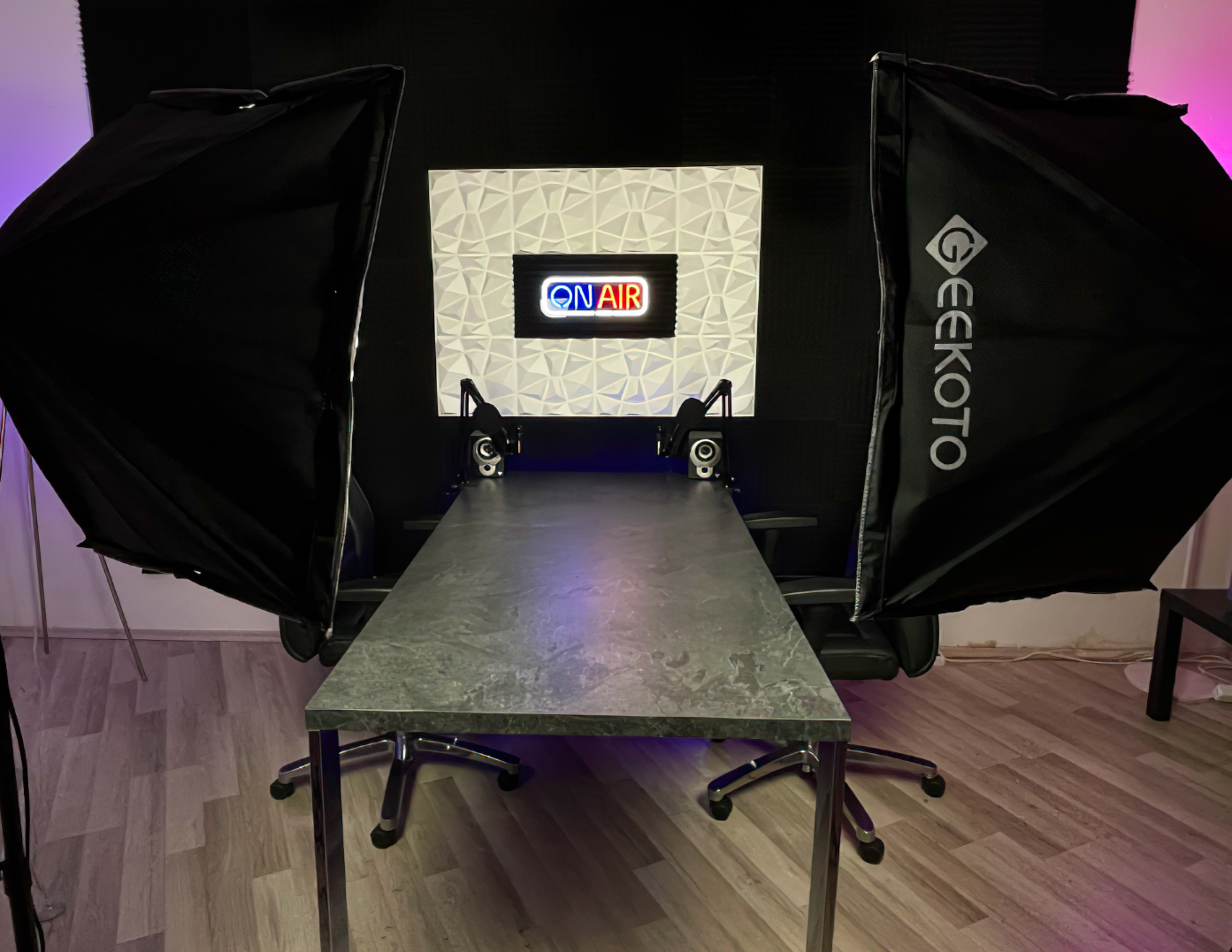A recording studio setup with a "ON AIR" sign, a gray table, and two softbox lights positioned on either side.