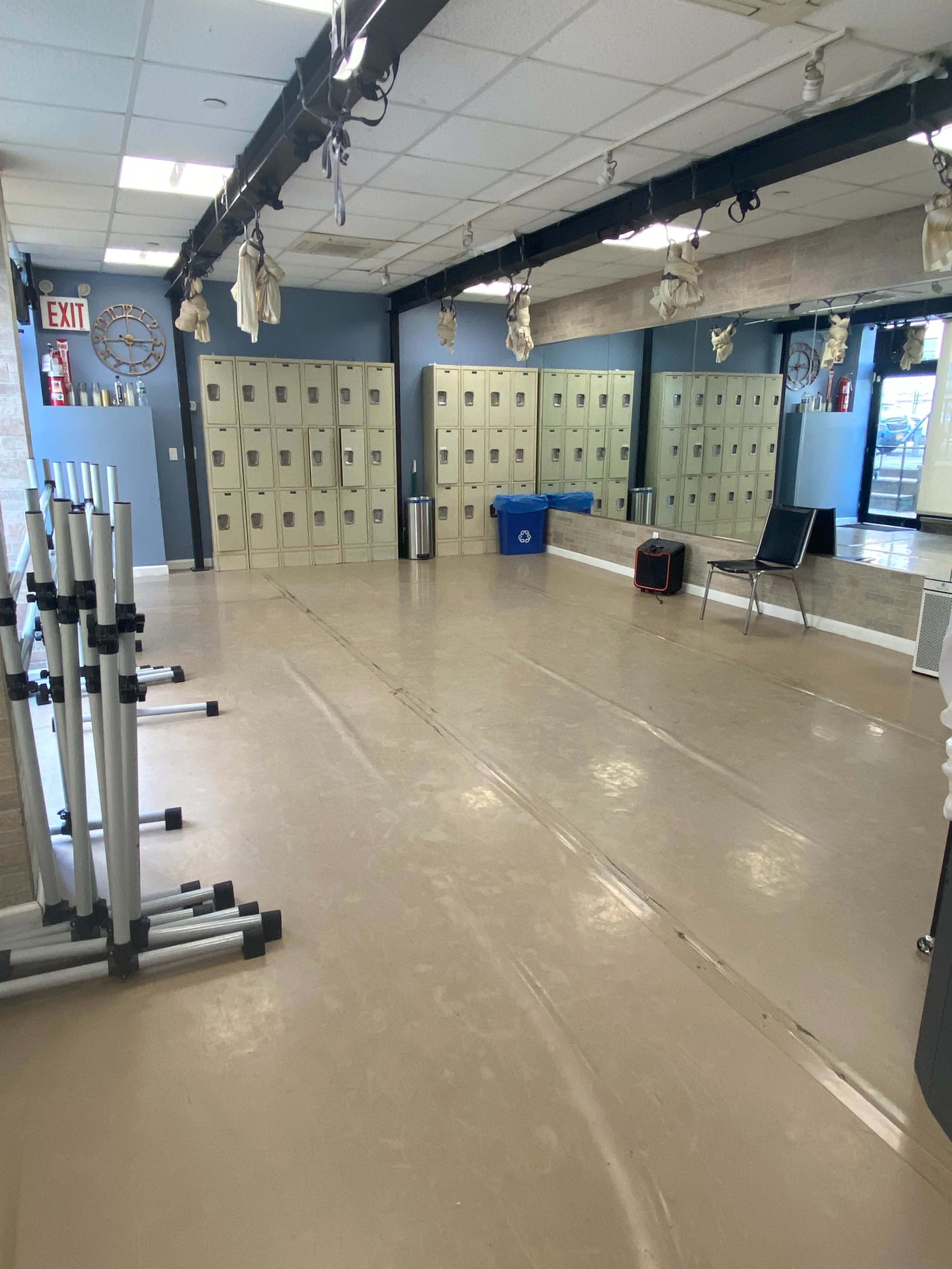 The image shows a spacious, well-lit studio with a polished floor, mirrored walls, and lockers lining one side.